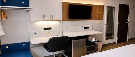 Habitación de hotel con cama, escritorio con silla, televisor de pantalla plana, armario y minibar.
