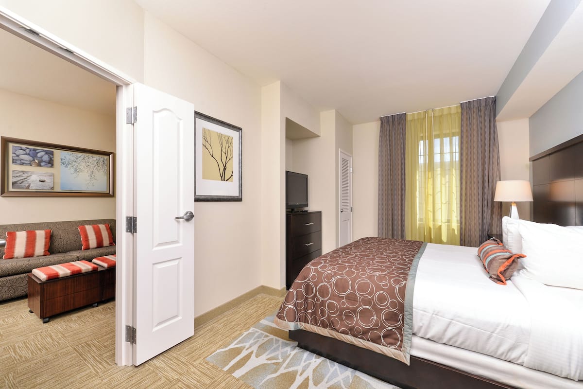 A hotel room with a bed, a sofa, a TV, and a door leading to another room.