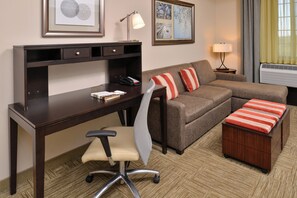 Habitación de hotel con escritorio, silla de oficina, sofá y un pequeño cofre de madera.
