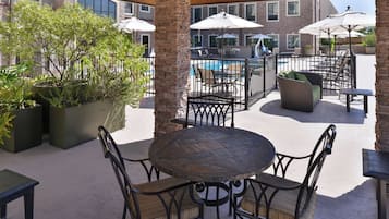 An outdoor patio area with a round table and chairs, surrounded by potted plants and umbrellas.