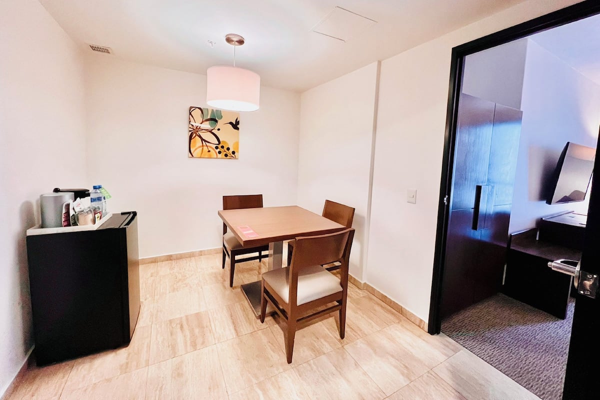 Una habitación pequeña y moderna con una mesa y sillas de madera, un mueble negro y un cuadro en la pared.