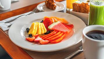 Un plato de desayuno con fruta, un croissant y un vaso de jugo verde.
