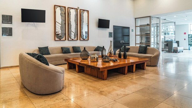 Un amplio salón con un sofá modular grande, una mesa de centro de madera y espejos decorativos.