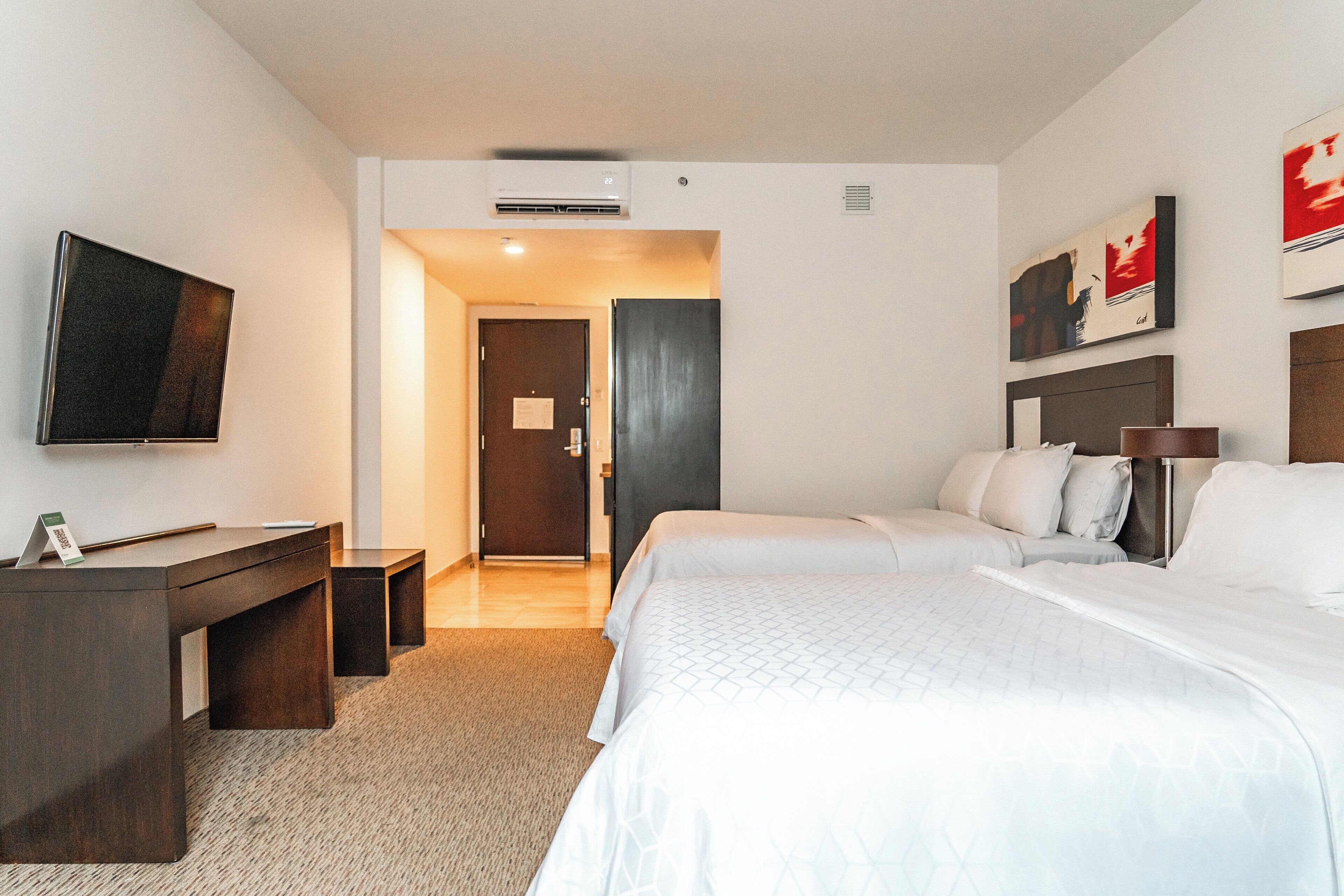 A hotel room with a bed, bedside tables, a desk, a flat-screen TV, and artwork on the walls.