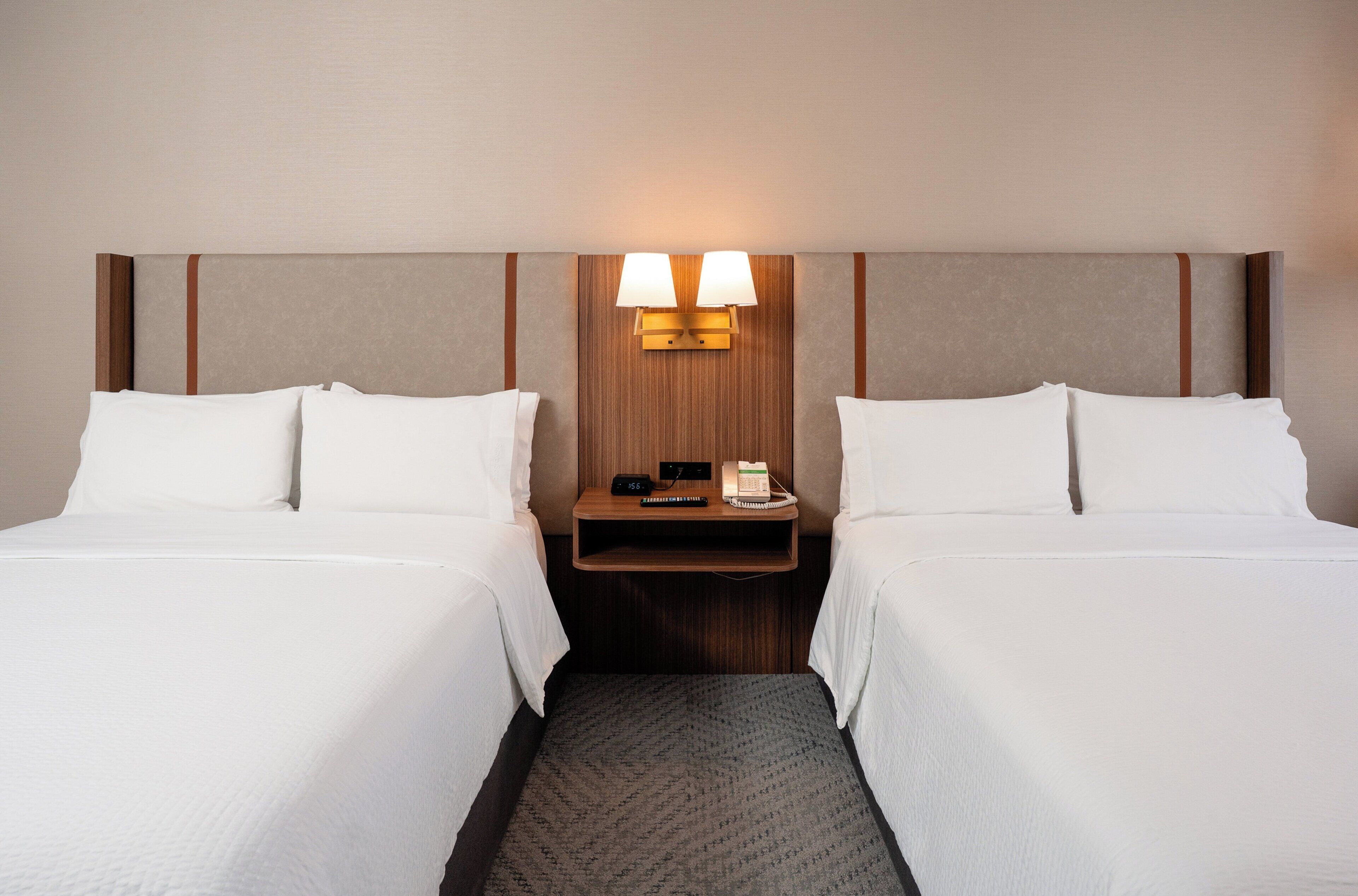 A hotel room with two beds, a nightstand with lamps, and a wooden headboard.