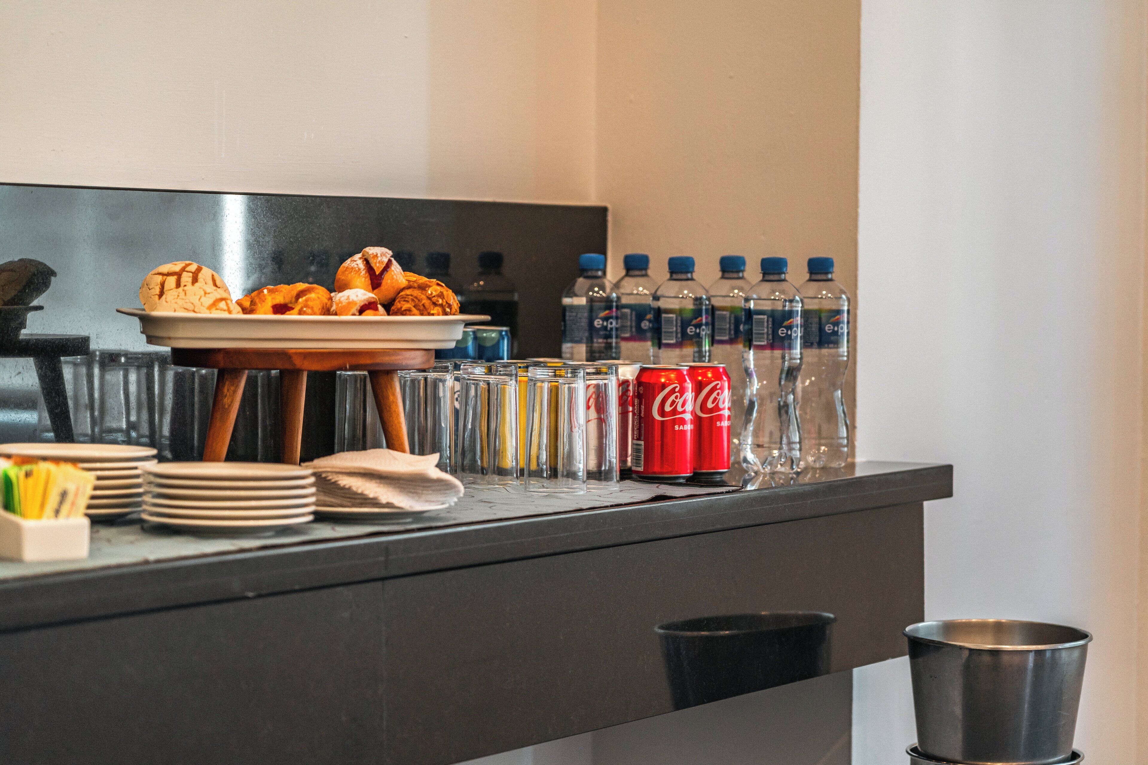 Een buffetopstelling met schalen eten, een schaal croissants, en verschillende flessen water en frisdrank.