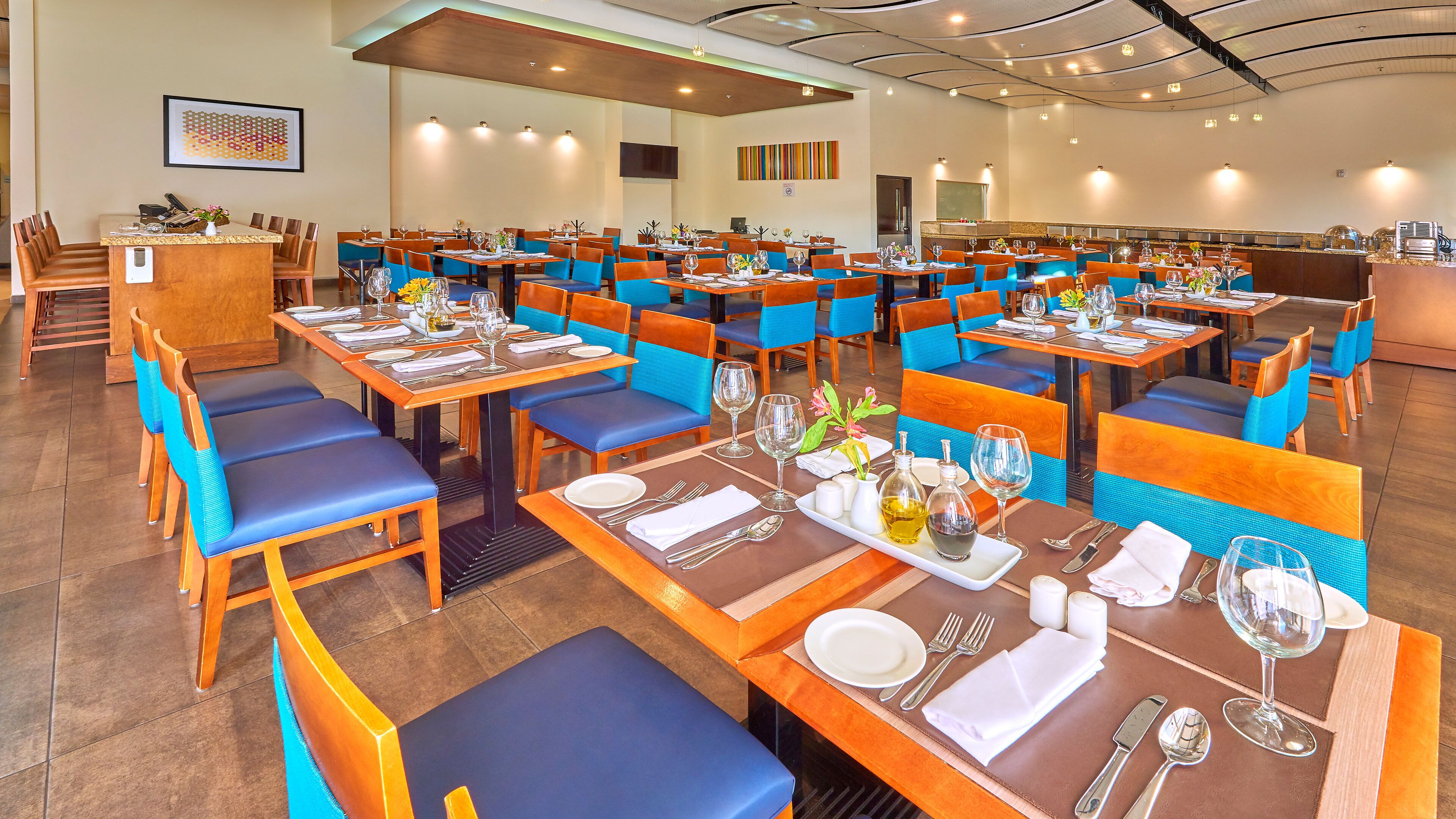 A restaurant with multiple dining tables, blue and orange chairs, and a variety of table settings.