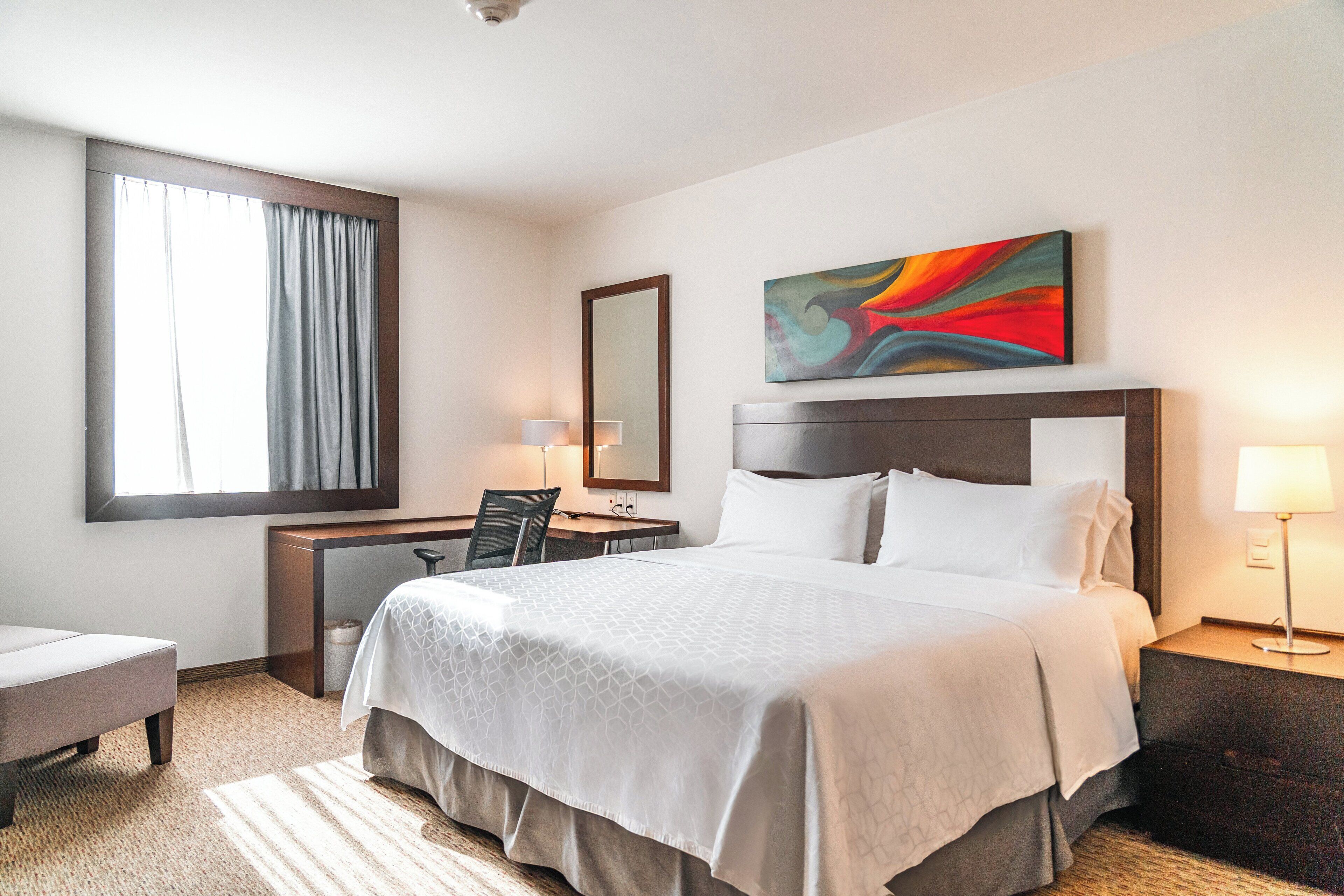 Una habitación de hotel con una cama grande, un escritorio, una silla y una lámpara de escritorio.