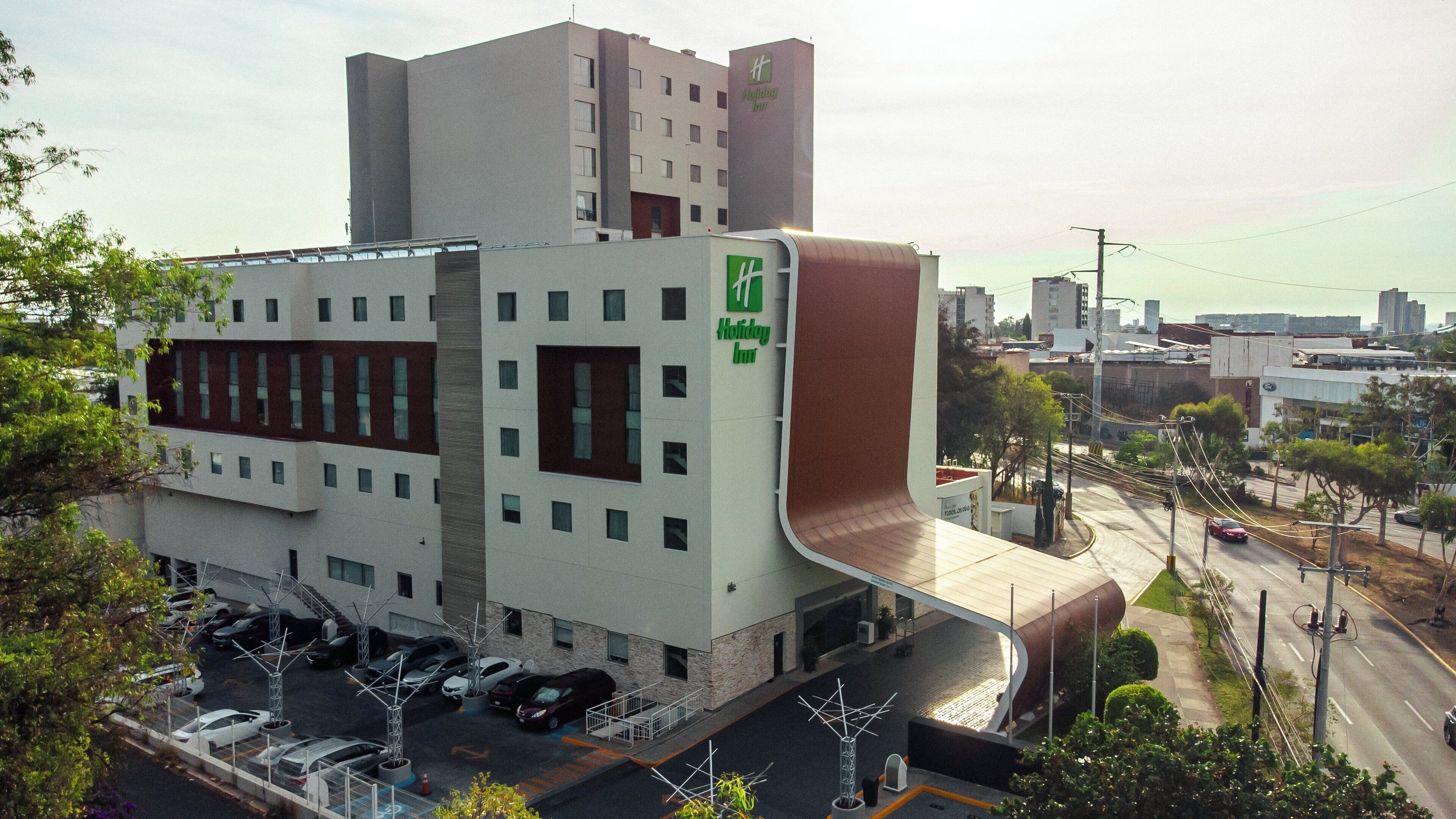 A Holiday Inn hotel with a modern design, featuring a parking lot and a street view with cars and buildings.