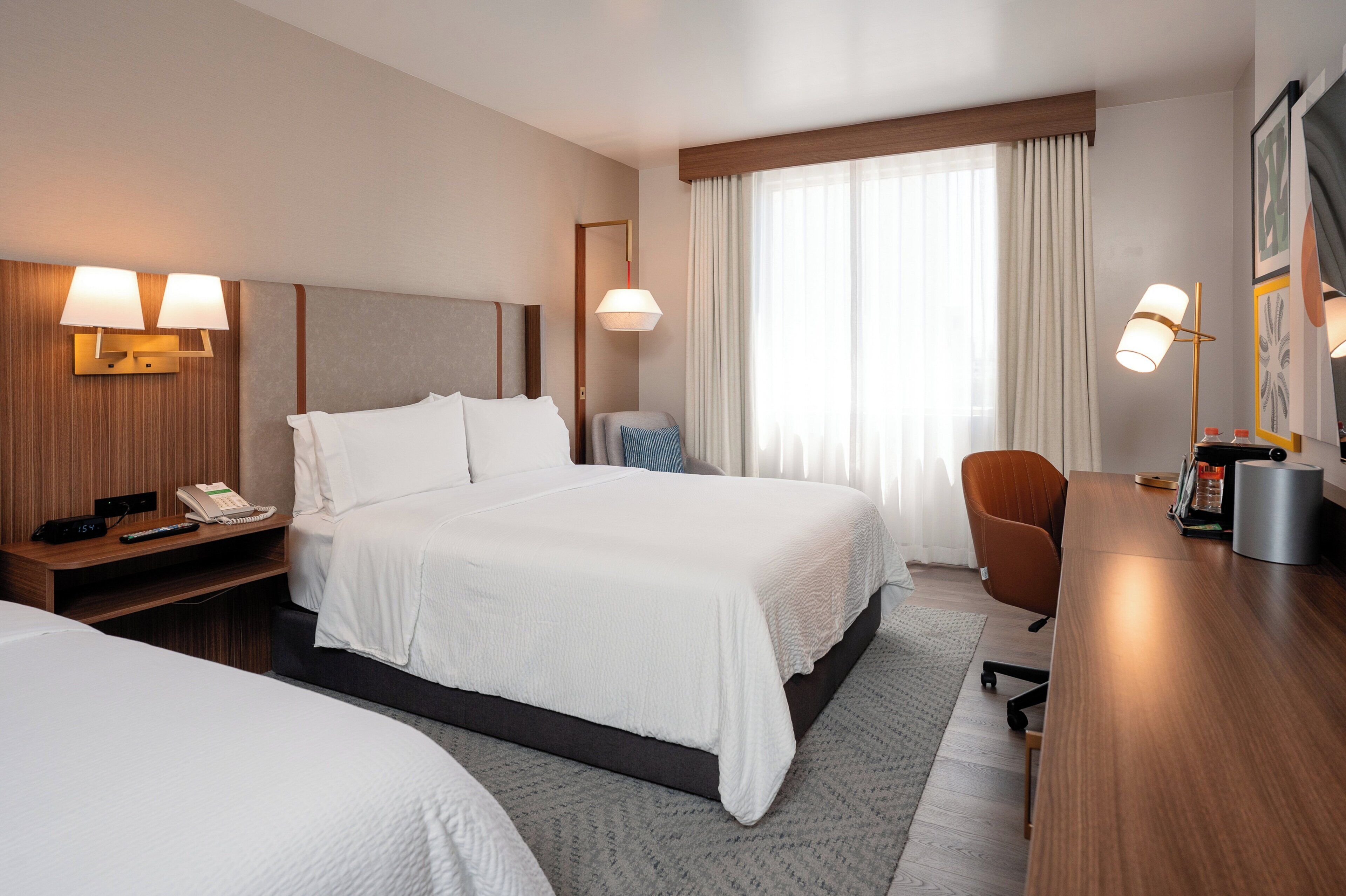 A hotel room with a large bed, bedside tables, a desk, a chair, and a window with curtains.