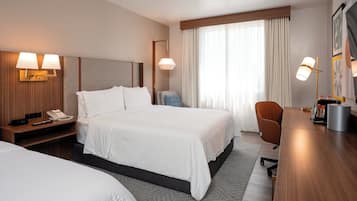 A hotel room with a large bed, bedside tables, a desk, a chair, and a window with curtains.