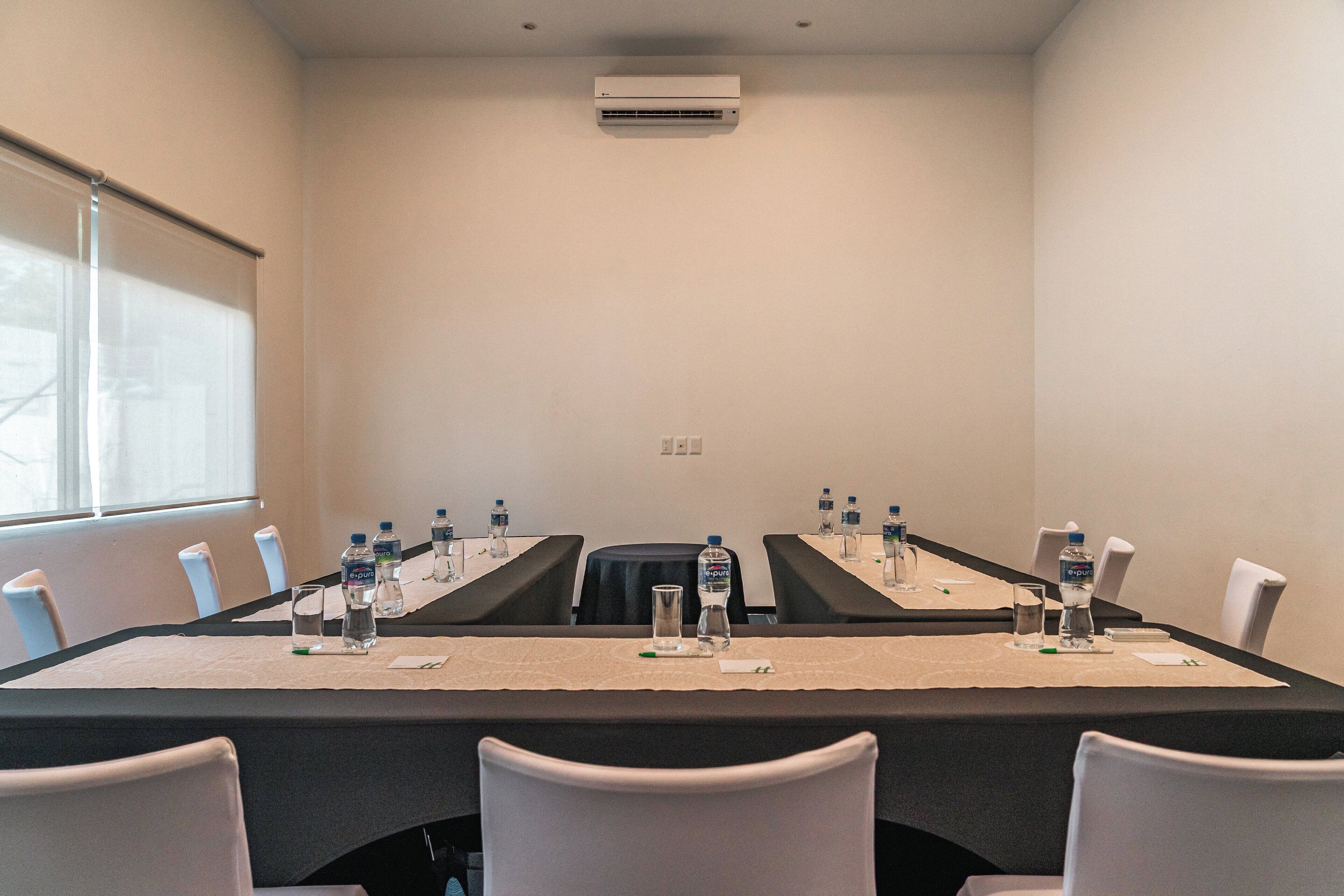 Un salón de conferencias con una larga mesa, sillas, botellas de agua y una pantalla para proyector.