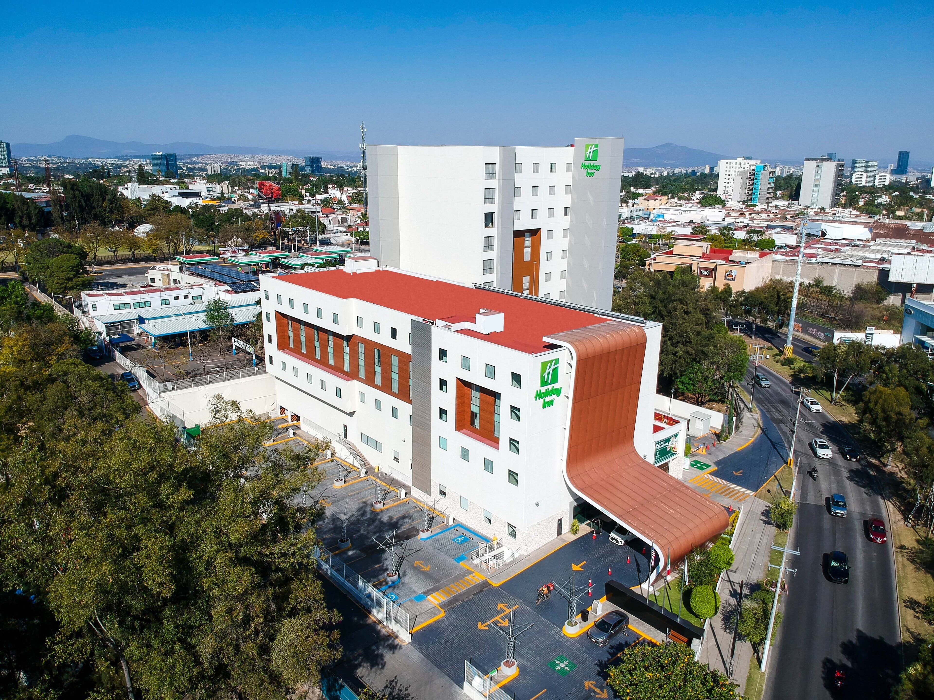 A Holiday Inn hotel with a modern design, featuring a prominent red roof and a large parking lot.