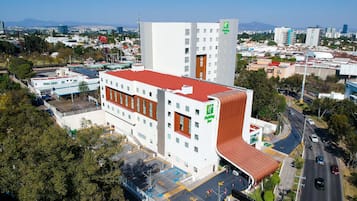 Un hotel Holiday Inn con diseño moderno, que destaca por su techo rojo prominente y un amplio estacionamiento.