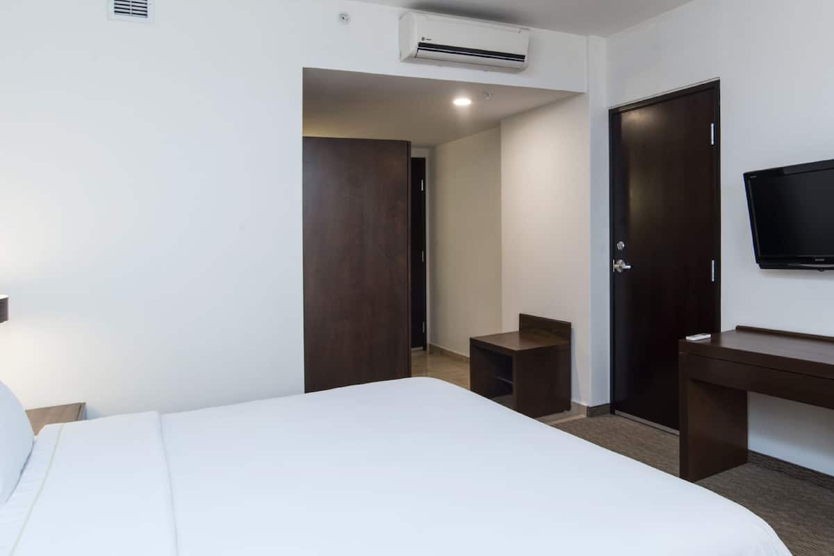 Una habitación de hotel con cama, escritorio, televisor y armario.