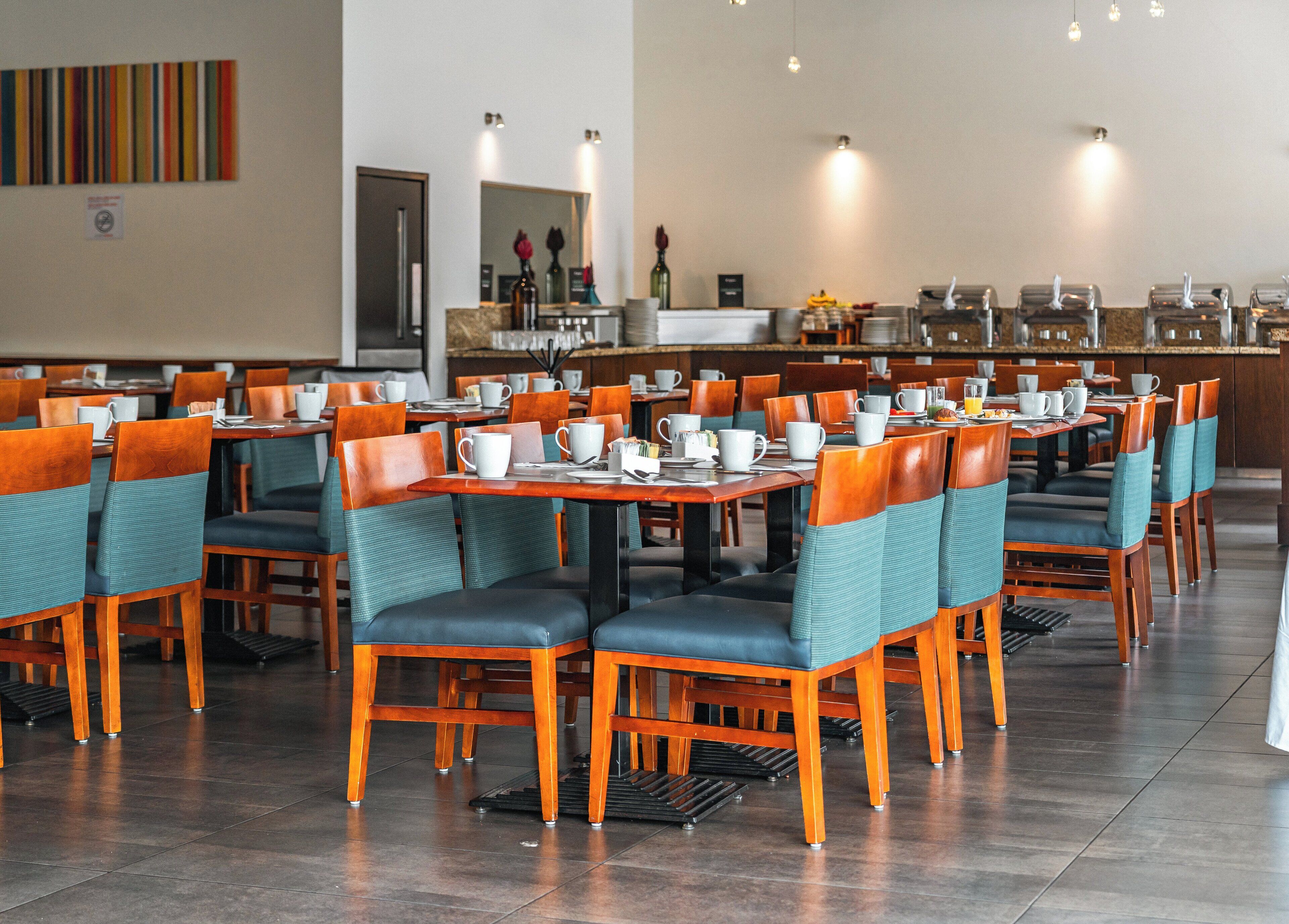 Un vaste espace dédié à la salle à manger, avec des tables et des chaises en bois, agrémenté de tasses et de soucoupes blanches, et un buffet en arrière-plan.
