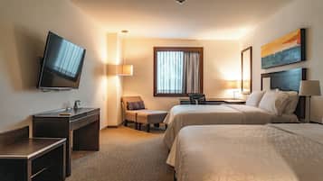 A hotel room with a TV, two beds, a desk, a chair, and a window with curtains.