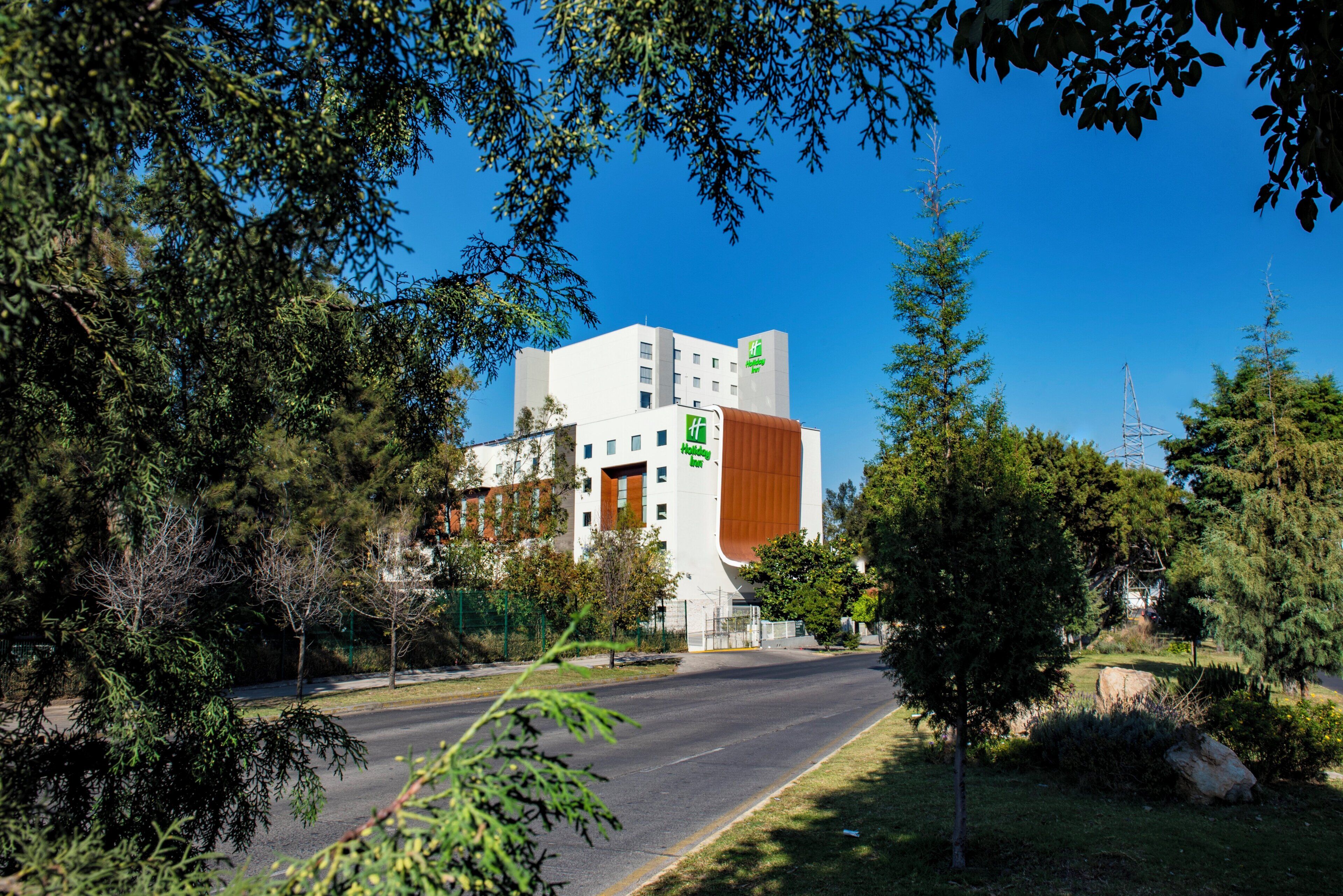 A modern building with a Holiday Inn sign, surrounded by trees and a clear sky.