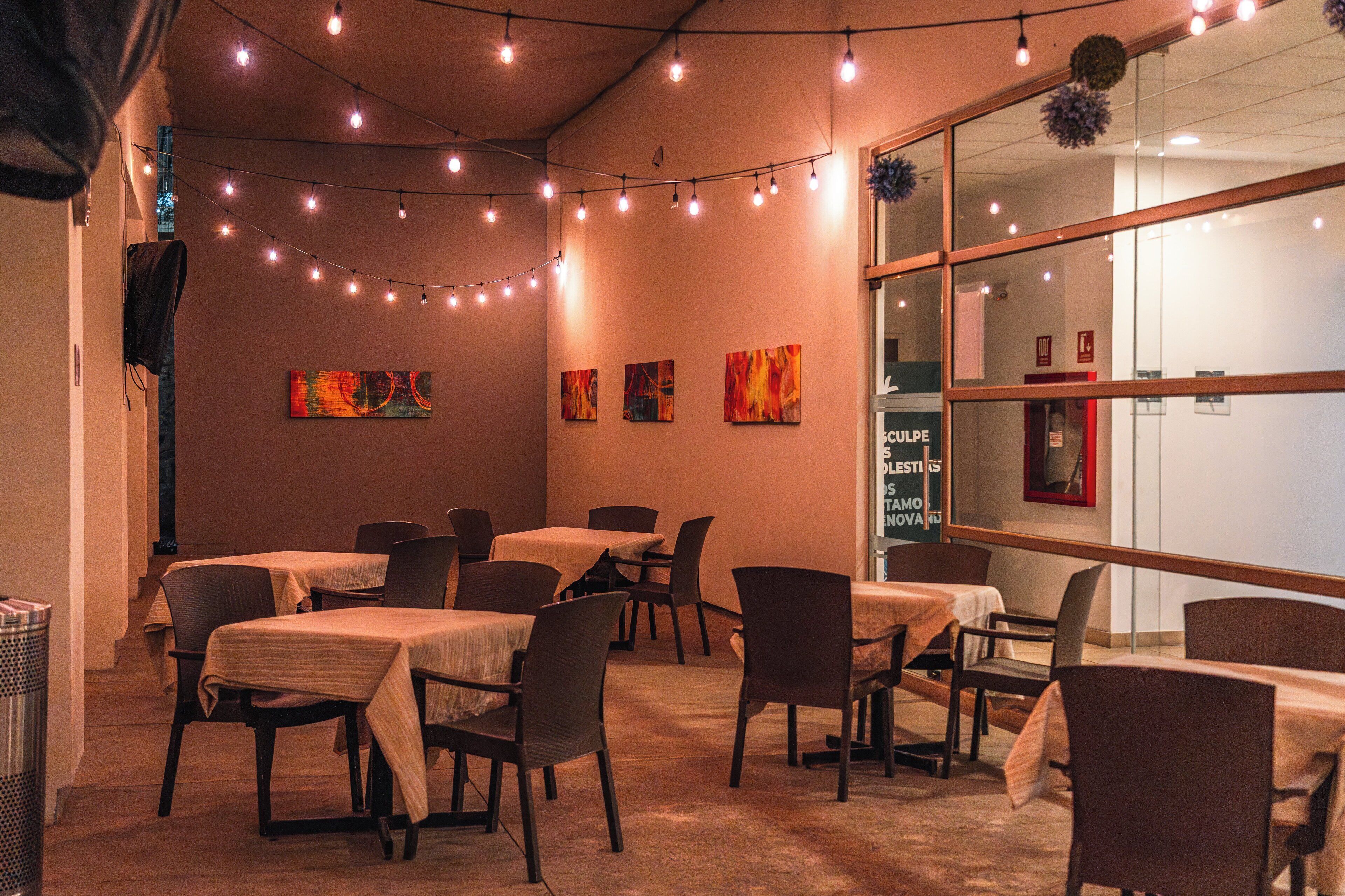 L’intérieur d’un restaurant, avec des tables et des chaises, des guirlandes lumineuses et des œuvres d’art accrochées aux murs.
