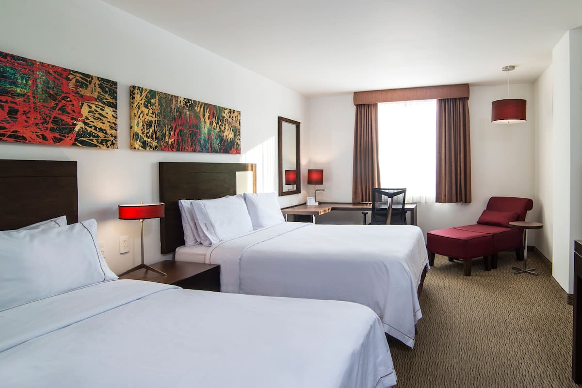 Habitación de hotel con dos camas, un escritorio, una silla y obras de arte en las paredes.