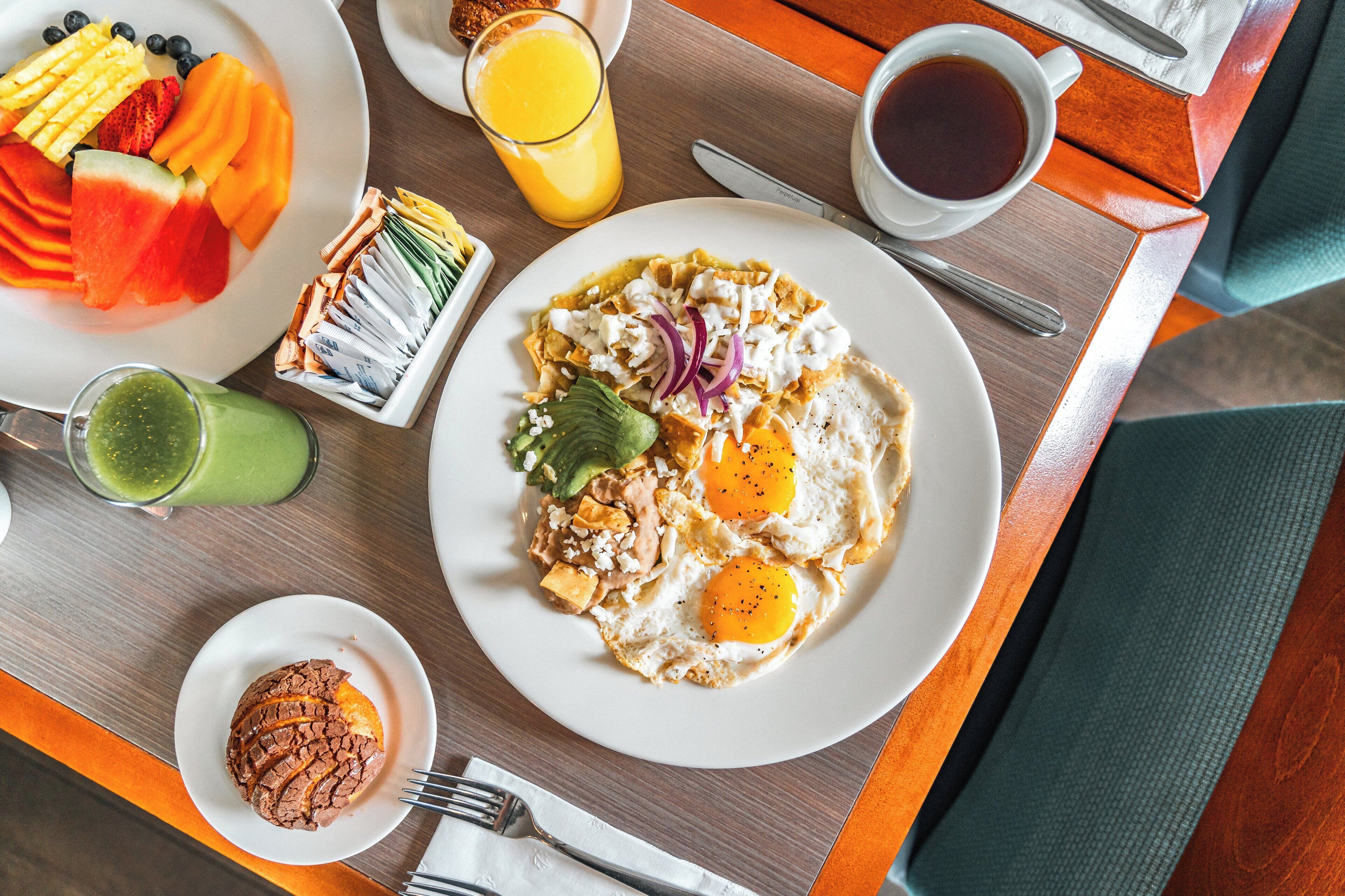 A breakfast setting with a plate of eggs, avocado, and red onions, a glass of orange juice, and a green smoothie on a wooden table.