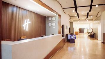 A reception area with a wooden panel wall, a reception desk, two clocks, and a television screen.