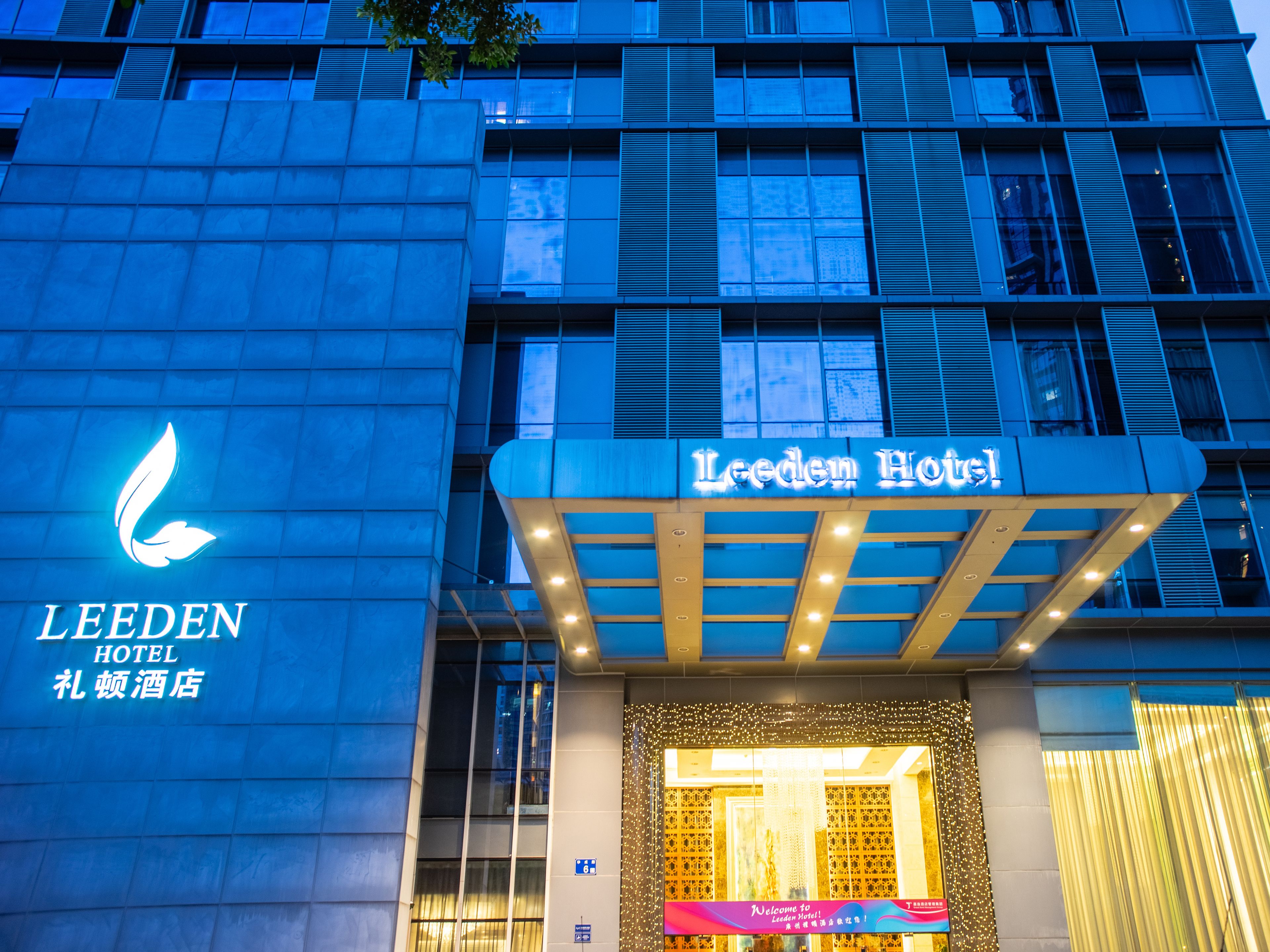 The exterior of the Leeden Hotel with a prominent illuminated sign and a modern facade.