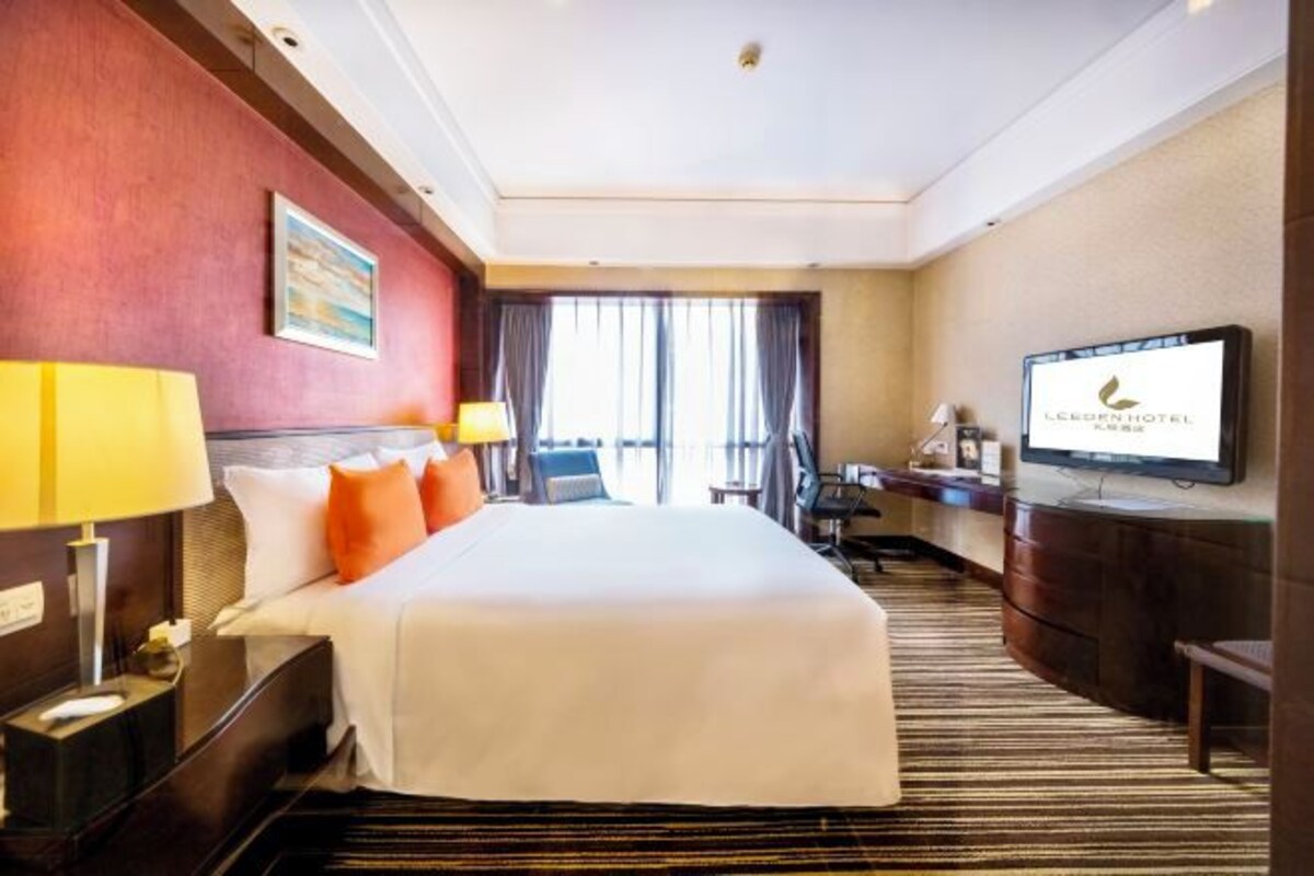 A hotel room with a bed, bedside lamps, a desk, a television, and a window with curtains.