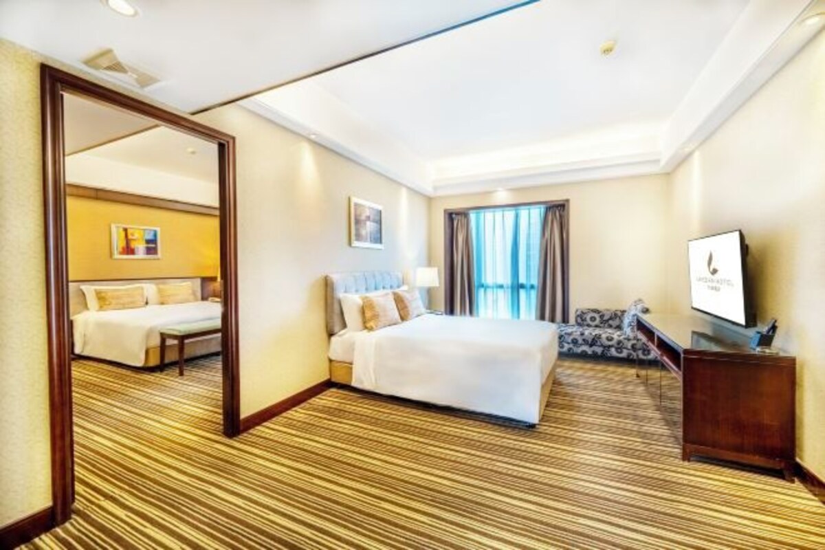 A hotel room with a large bed, a sofa, a TV, and a mirror.