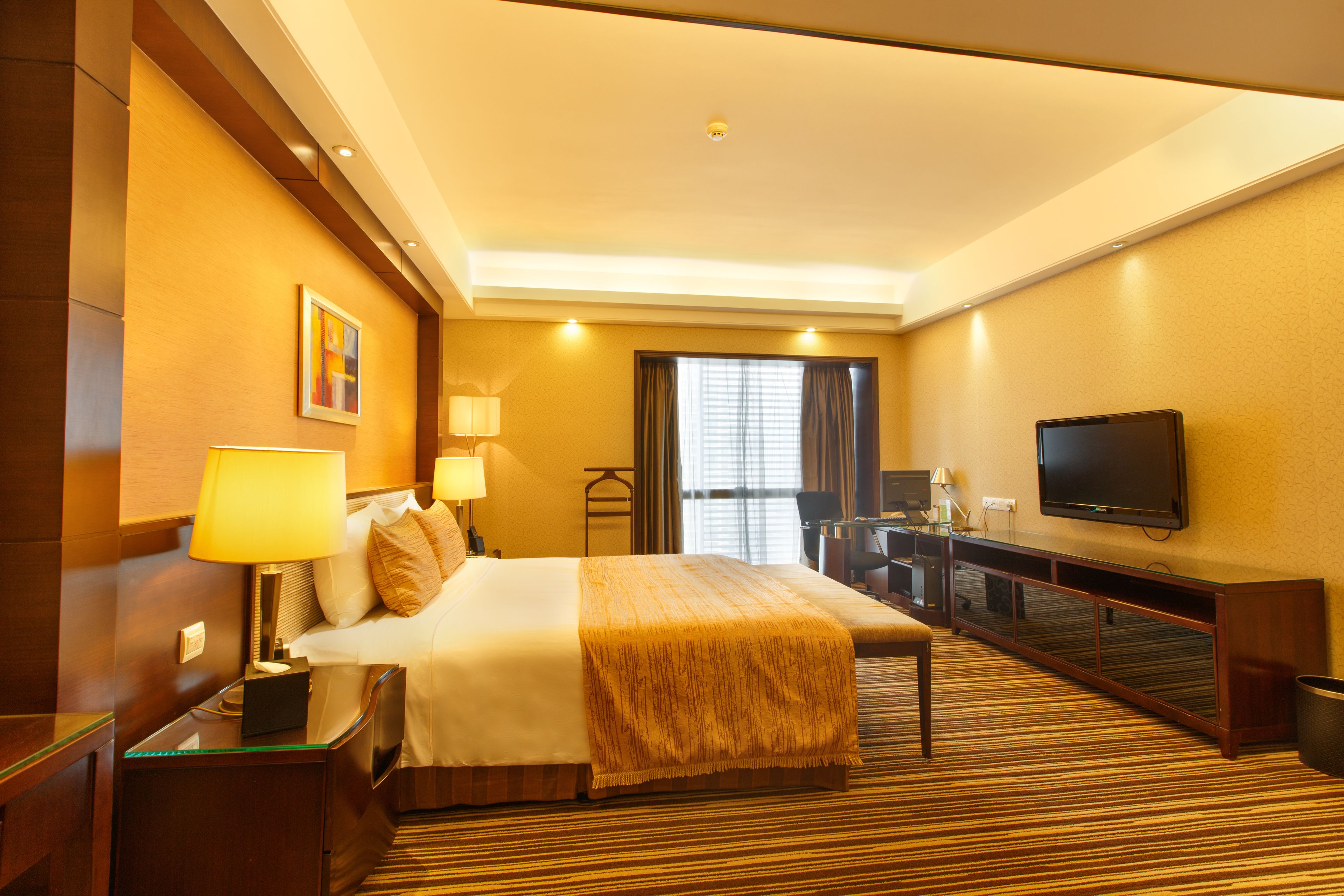 A hotel room with a bed, bedside tables, a TV, a desk, and a window with curtains.