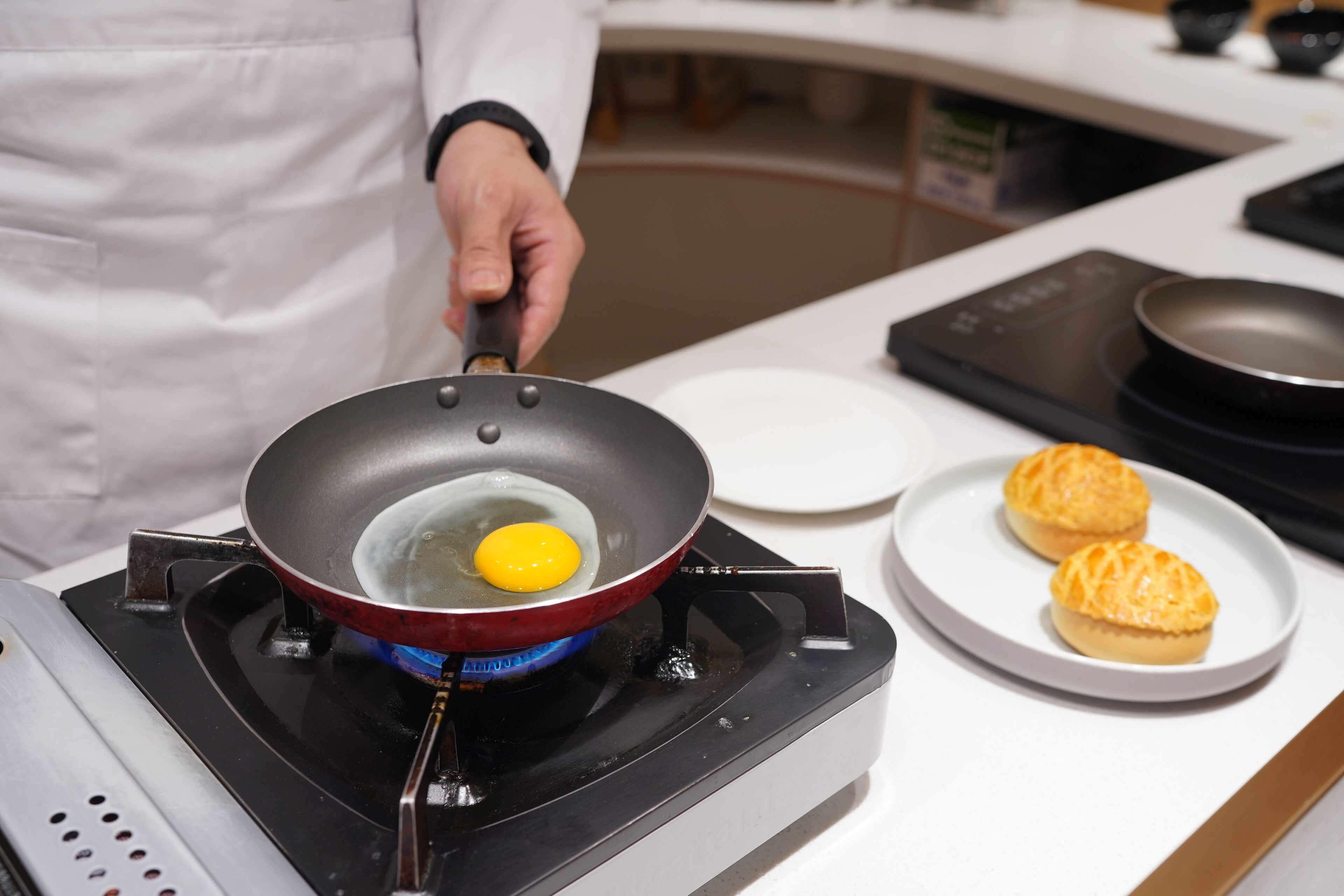 Una cocina con estufa, una sartén con un huevo y un plato con pasteles.
