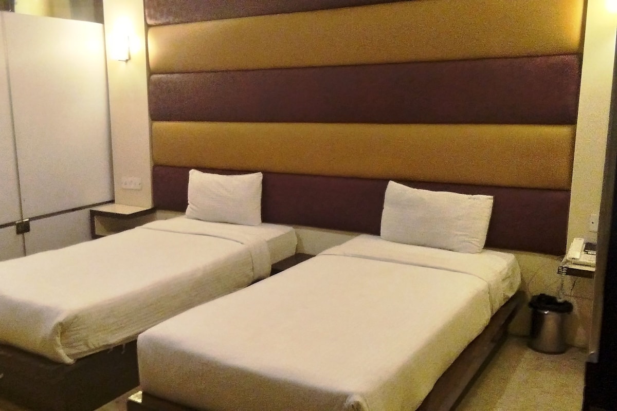 A hotel room with two single beds, a nightstand, a trash can, and a wall-mounted light.