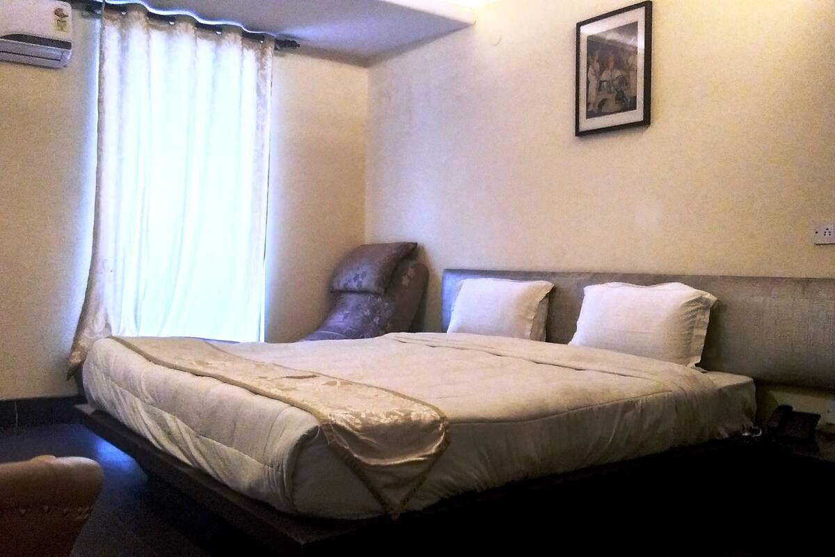A hotel room with a bed, a chair, a picture on the wall, and a window with curtains.