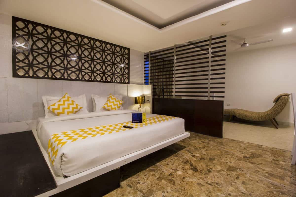 A modern hotel room with a bed, a nightstand, a decorative wall panel, a ceiling fan, and a unique seating area.
