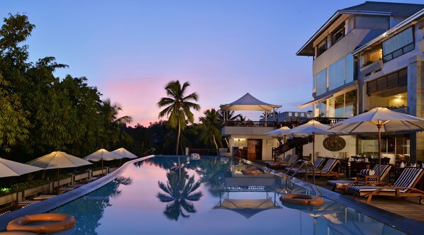 Relax by the serene pool surrounded by palm trees and lush greenery, with lounge chairs and umbrellas at your disposal.