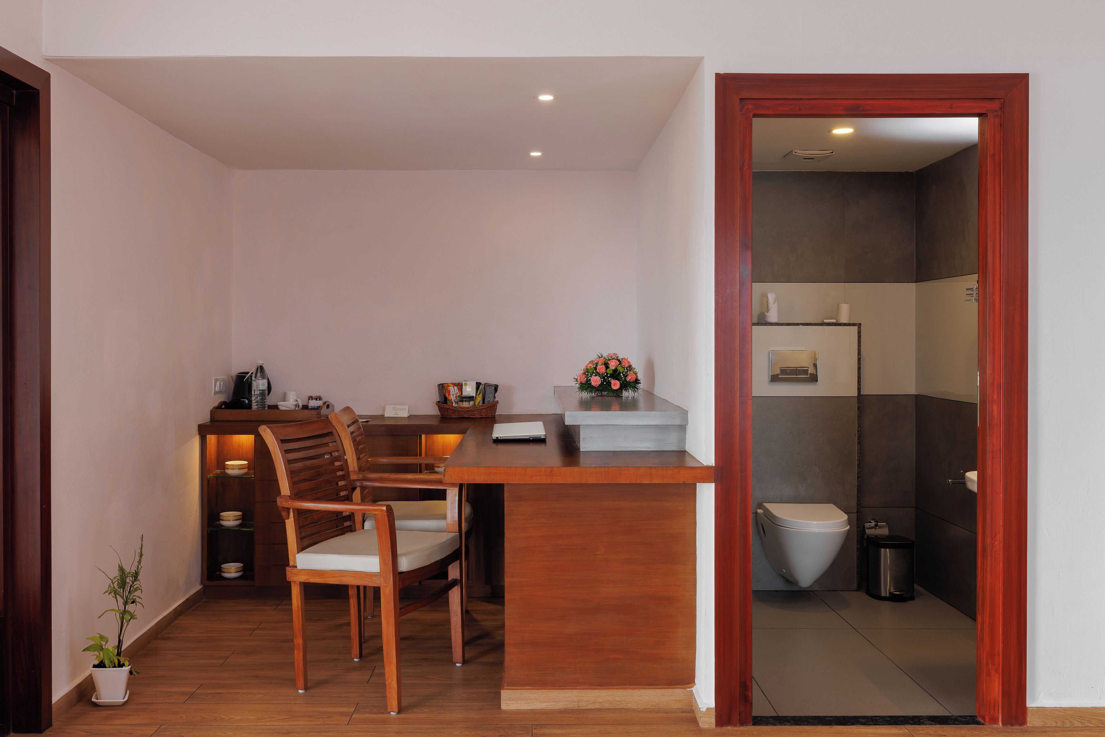 Un ambiente compatto con un tavolo e sedie in legno, una piccola cucina e un bagno separato visibile attraverso una porta aperta.