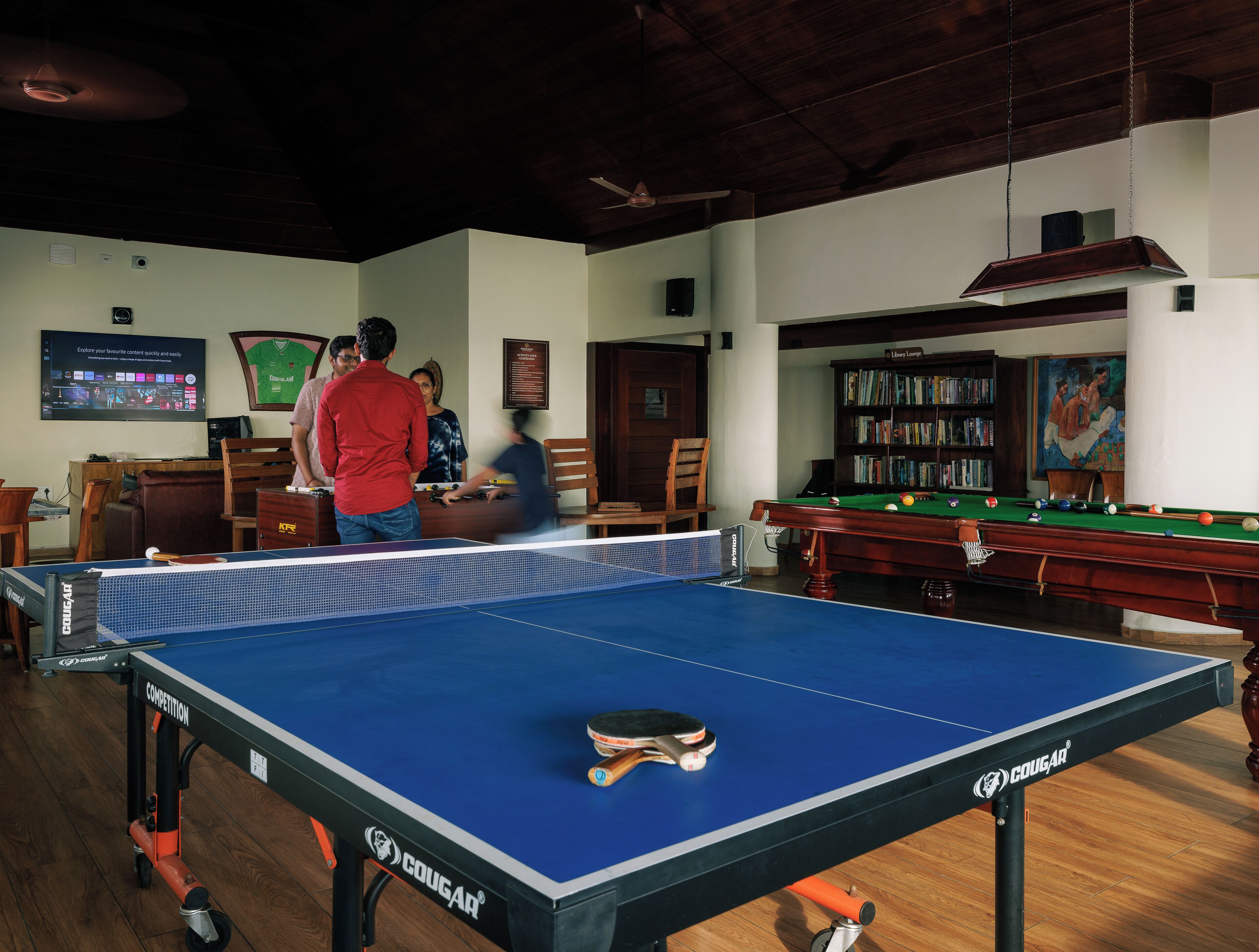 A billiards table with a blue cloth, a pool table, and a library in the background.