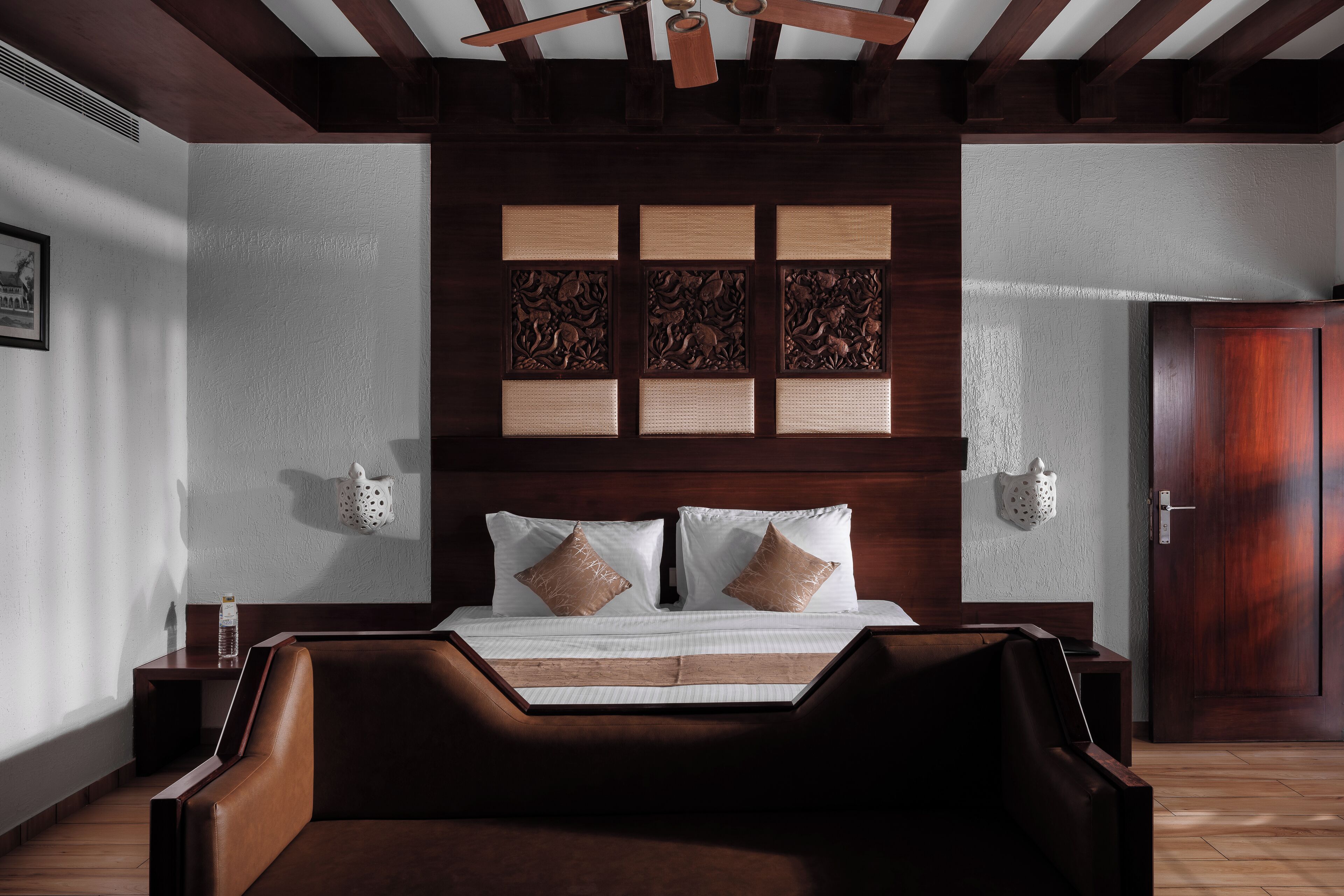 A bedroom with a wooden headboard, a bed with white linens and two decorative pillows, a wooden bench at the foot of the bed, and a wooden door.