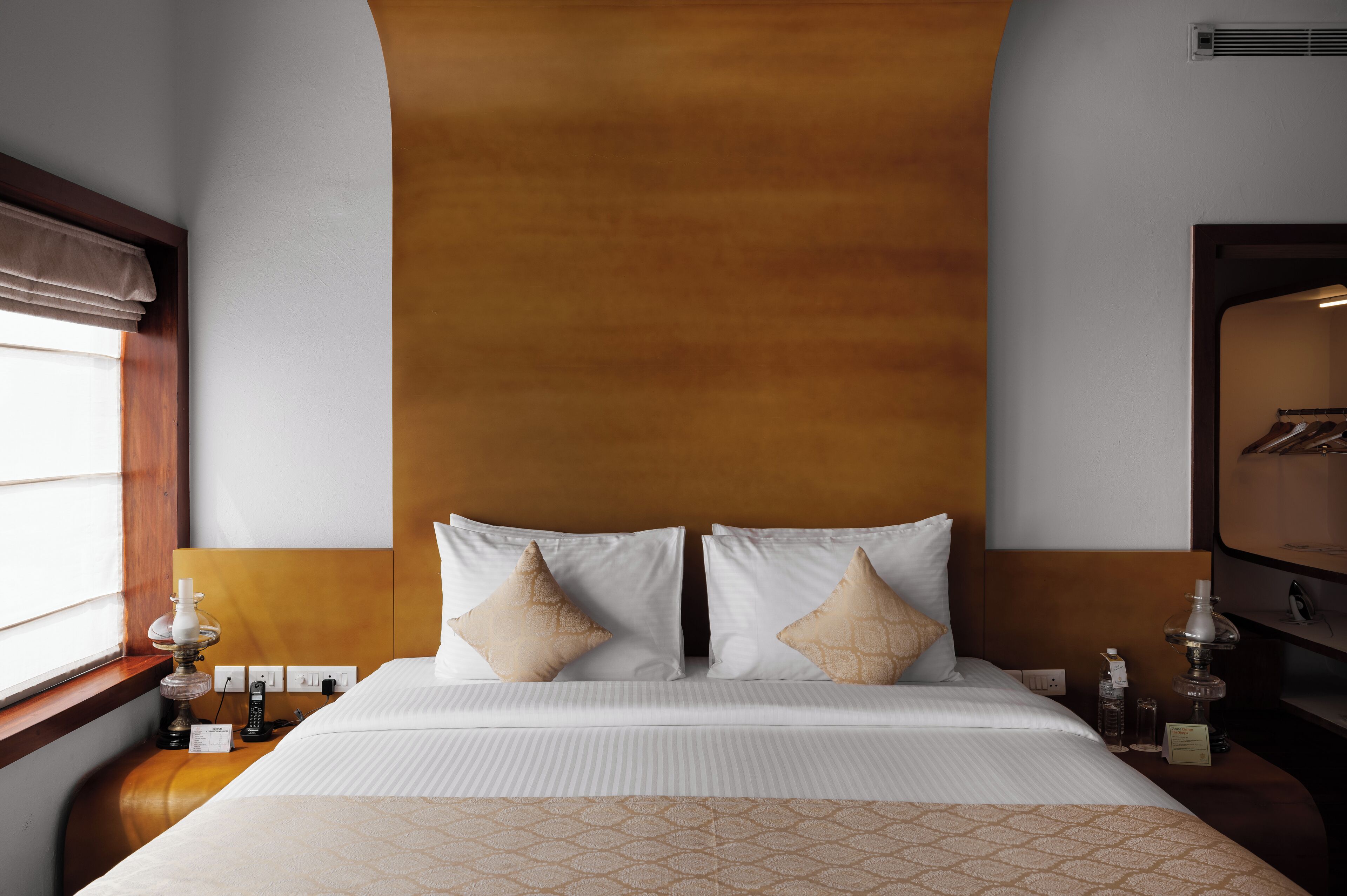 A hotel room with a large bed, two bedside tables, a nightstand, a lamp, a telephone, and a wall-mounted heater.
