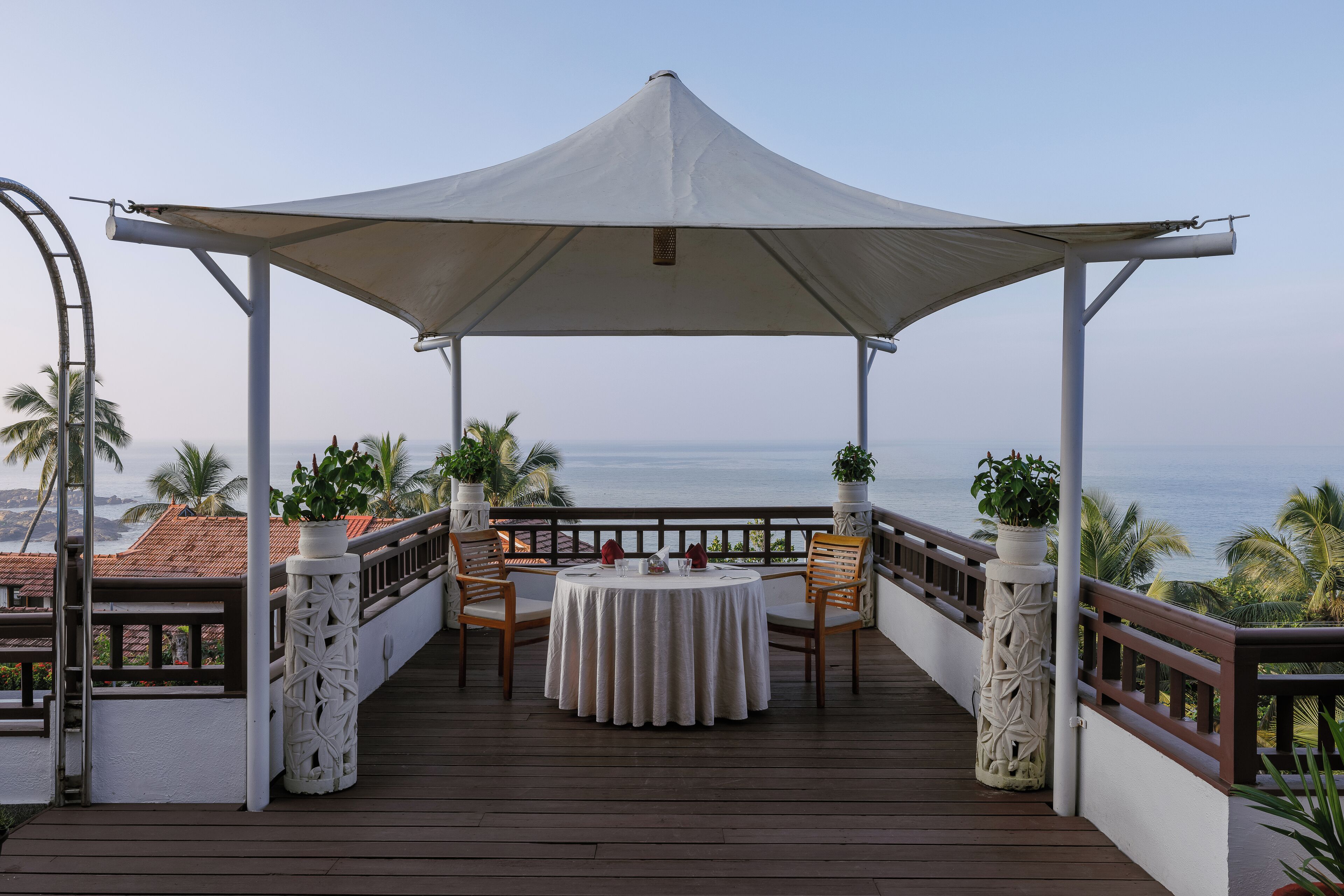 A covered outdoor seating area with a table and chairs, overlooking the ocean.