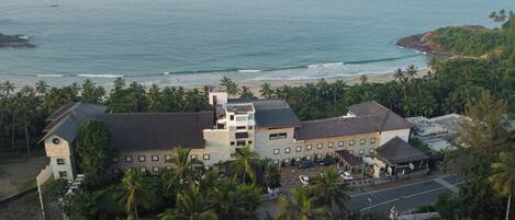 A large building with multiple floors, surrounded by palm trees and a beach.