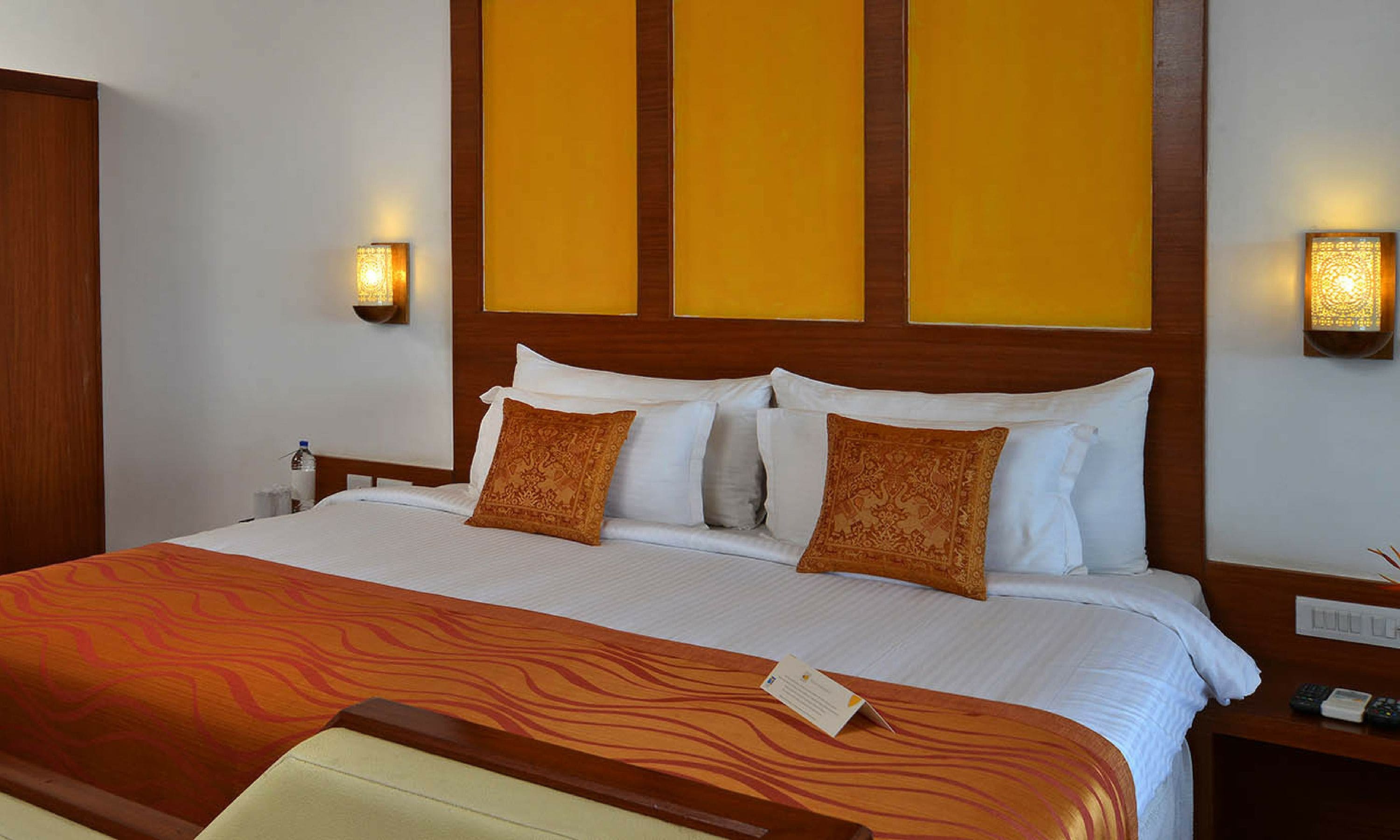 Una habitación de hotel con una cama grande, dos lámparas fijadas a la pared y un cabecero de madera.