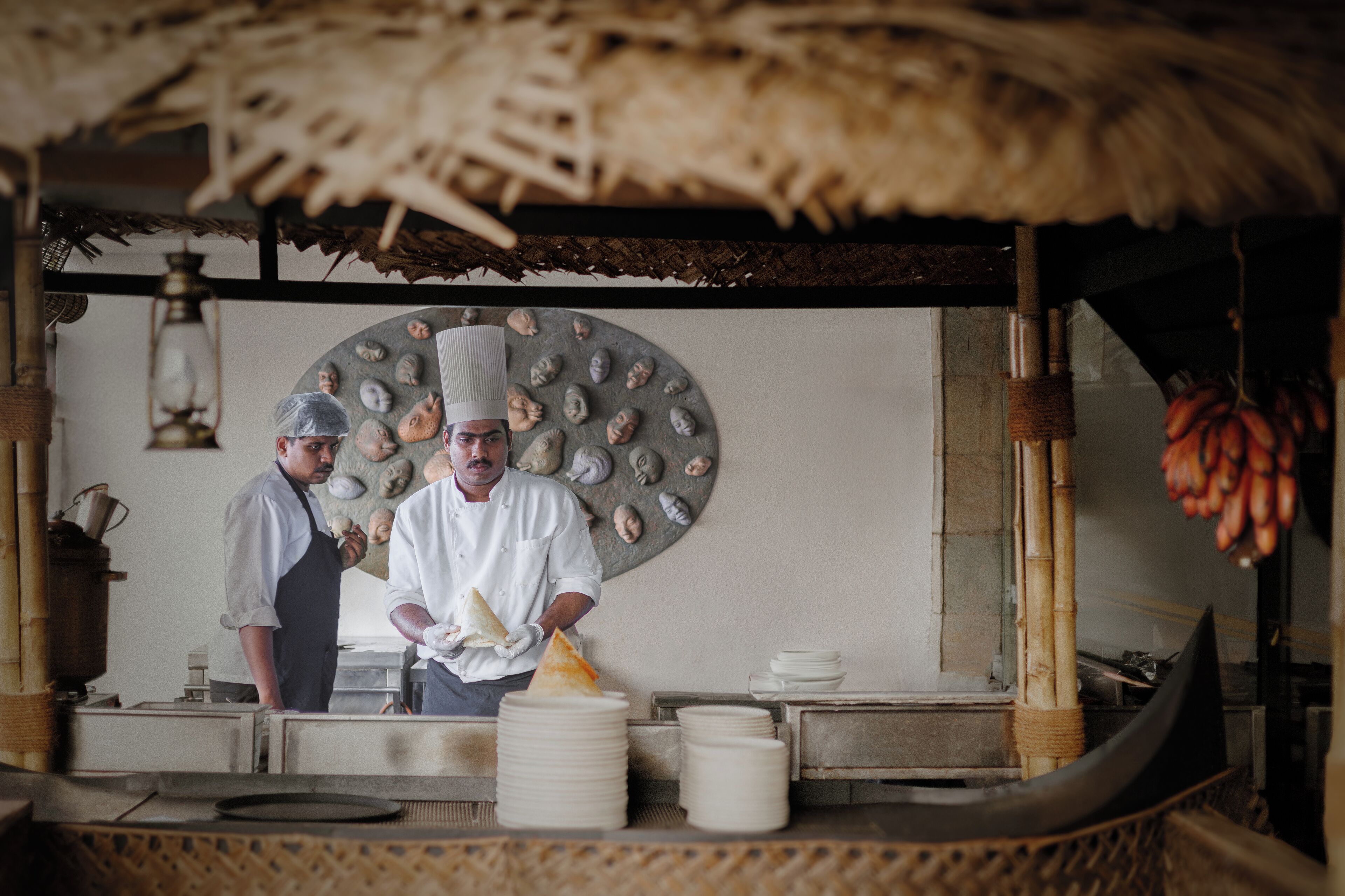 A chef preparing food in a kitchen with a rustic thatched roof and a decorative wall.