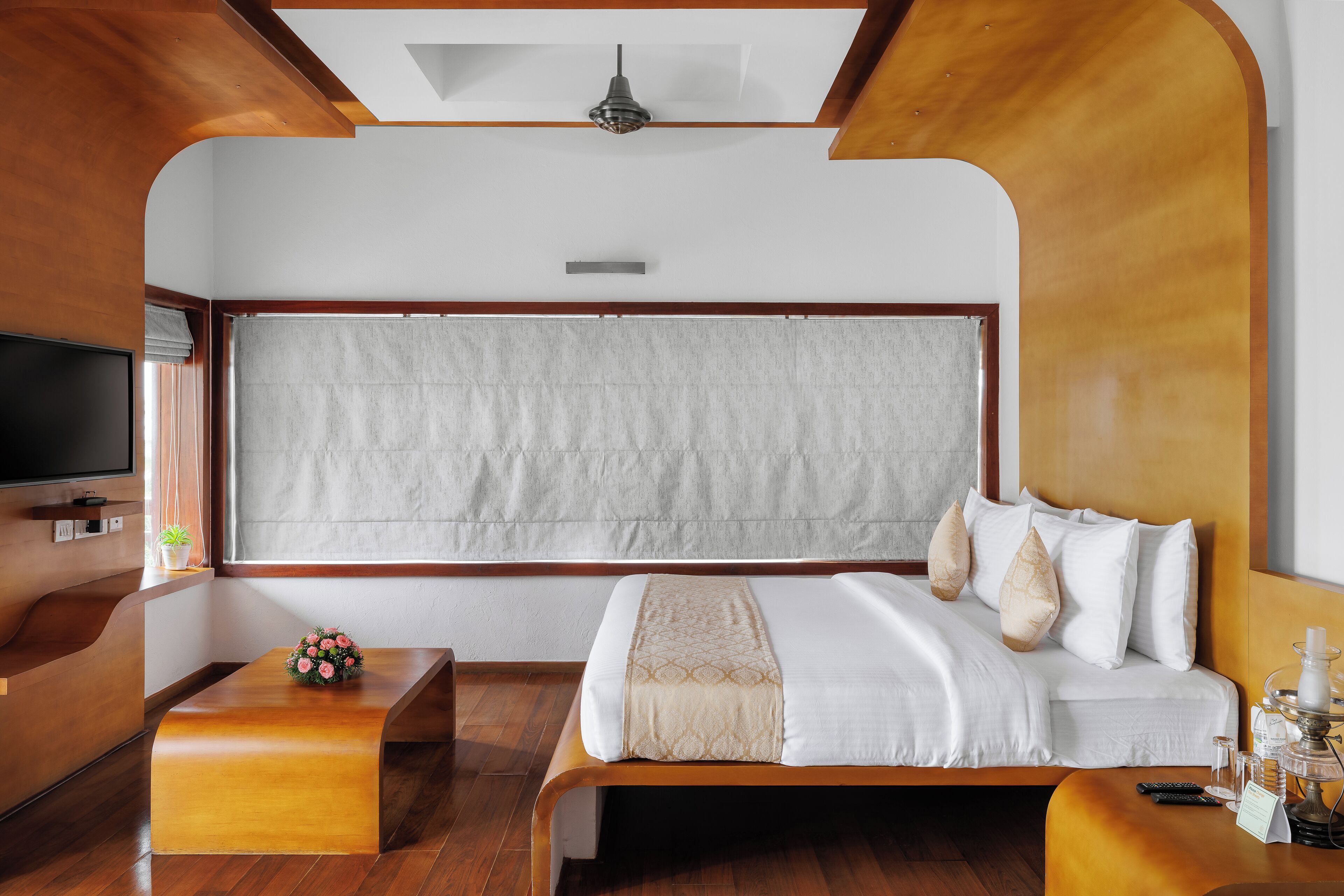 Une chambre d’hôtel moderne avec un grand lit, un banc en bois, une télévision et une grande fenêtre avec des rideaux.