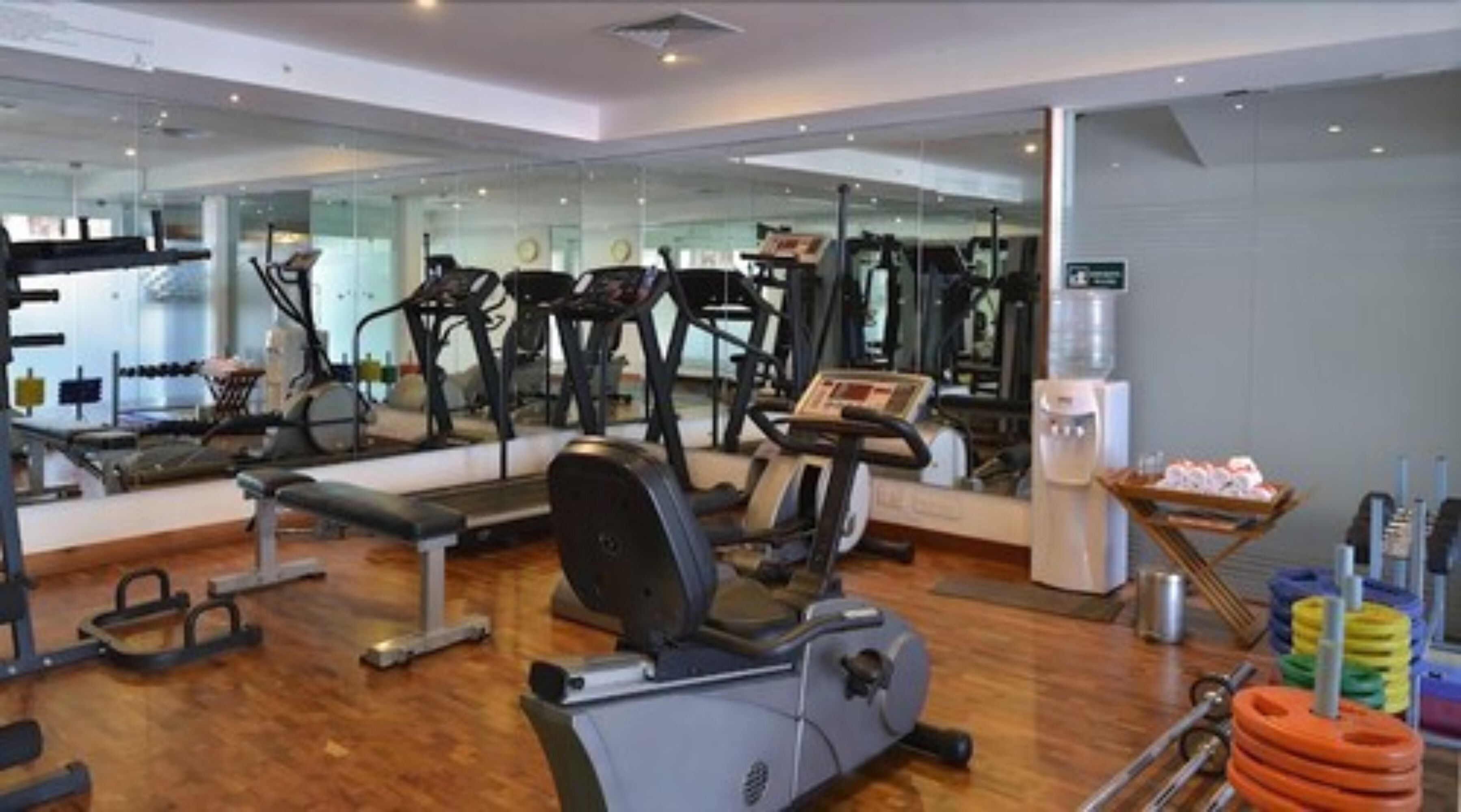 A gym with cardio machines, free weights, and a mirrored wall.