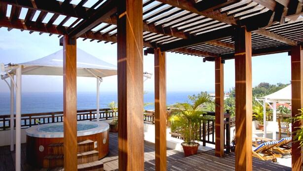 Una terraza de madera con un jacuzzi, sillas de descanso y vista al océano.