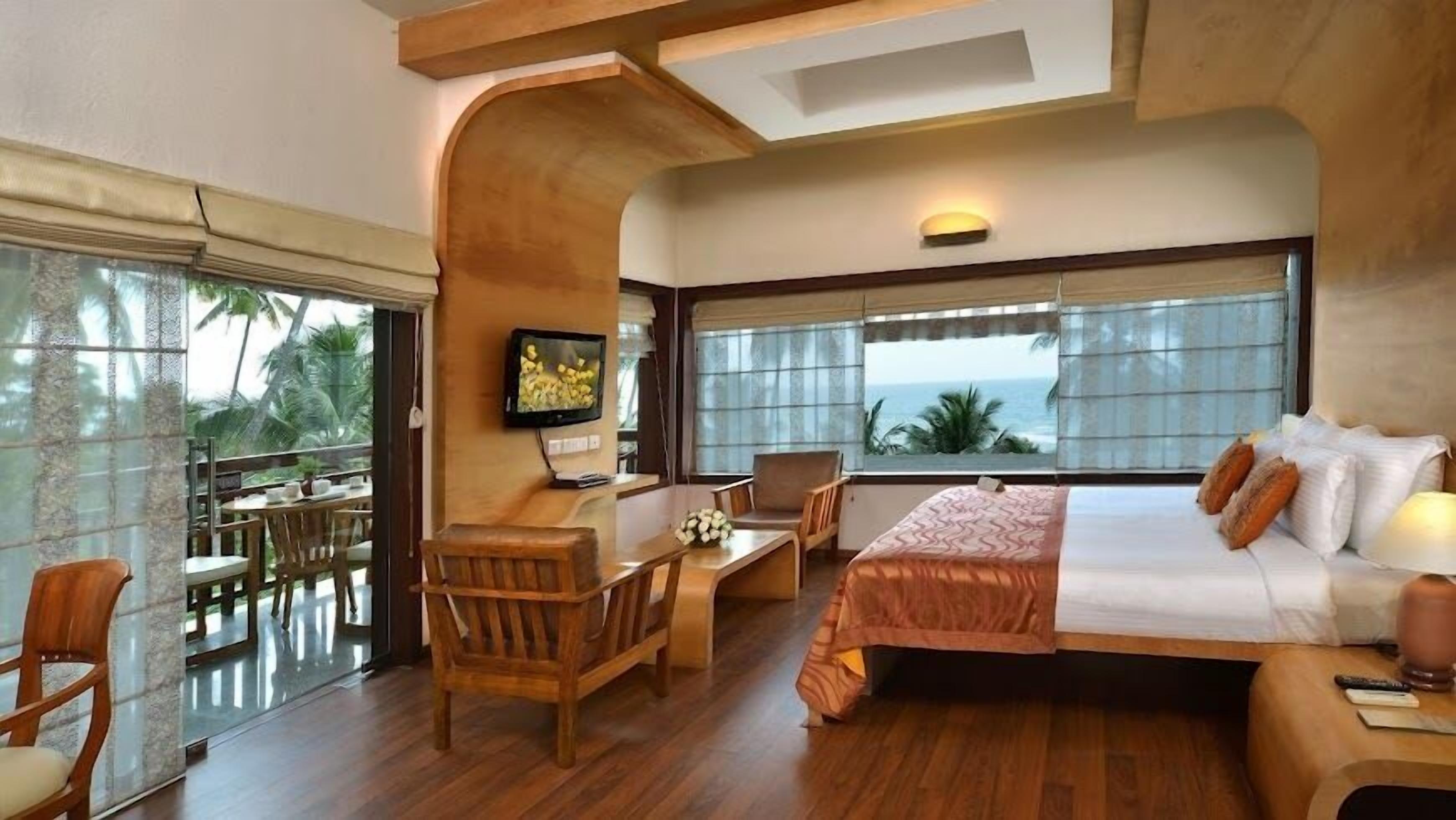 A hotel room with a bed, desk, chair, and a TV. There is a balcony with a table and chairs.