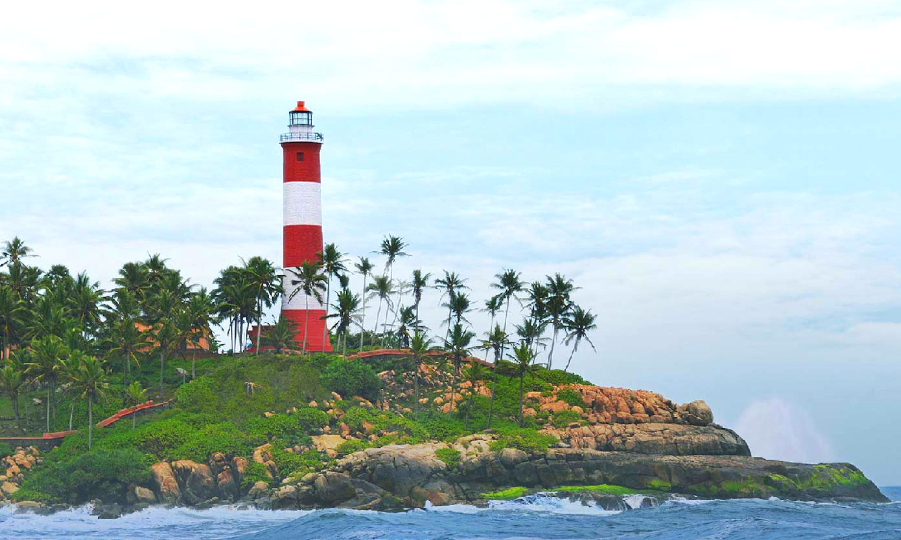 Un phare perché sur un promontoire rocheux, entouré de palmiers et bercé par les vagues de l’océan.