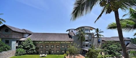 A large building with multiple floors, a courtyard with a lawn and seating area, and surrounding palm trees.