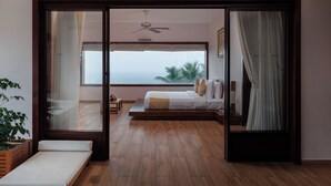 Un dormitorio con una ventana grande, una cama, un ventilador de techo y vistas a palmeras.